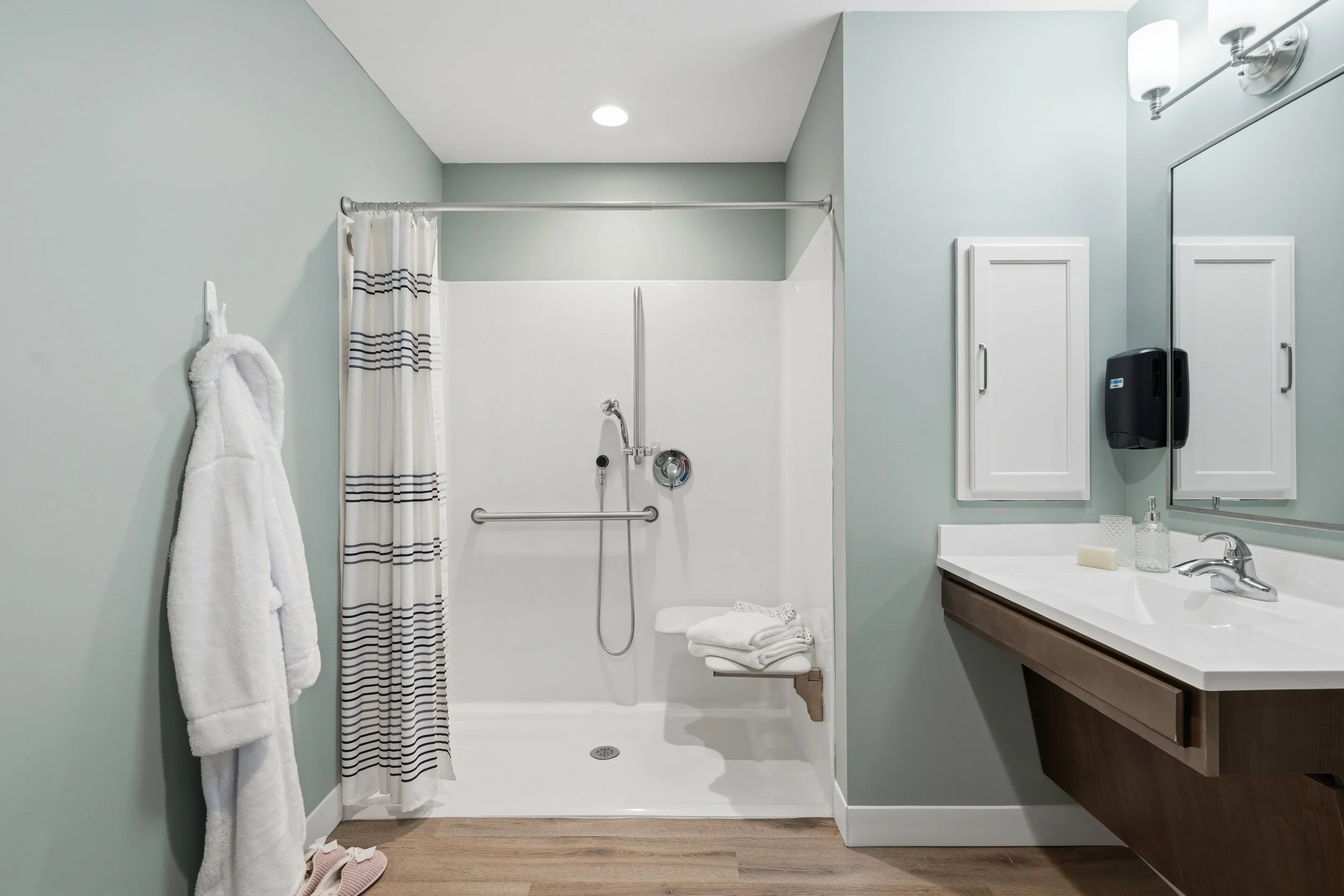 Bathroom with a shower, striped shower curtain, white towel, bathroom sink with soap and paper towel dispenser