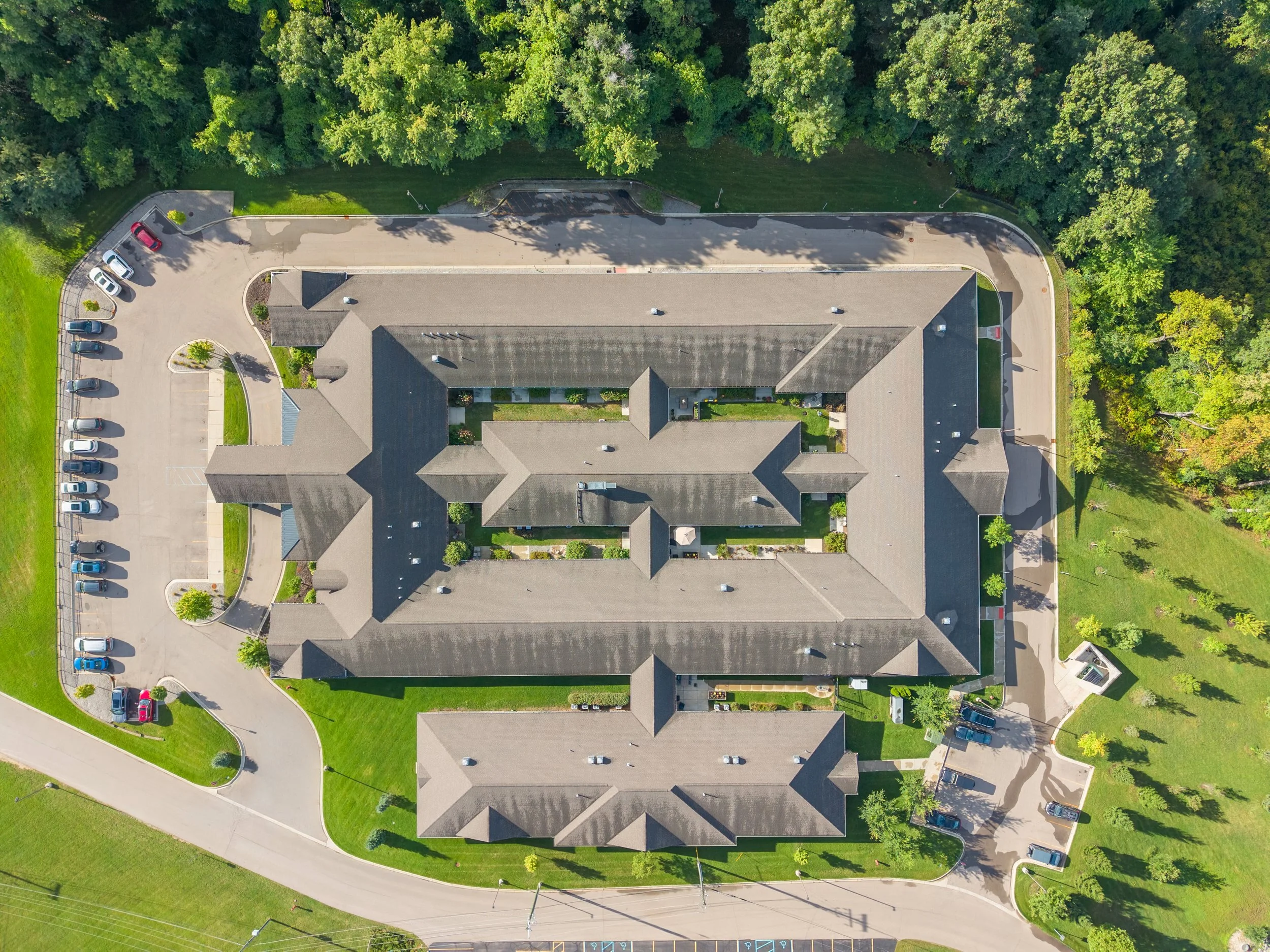 An aerial view of a large residential complex with several buildings, parking lots, green lawns, and surrounding trees.