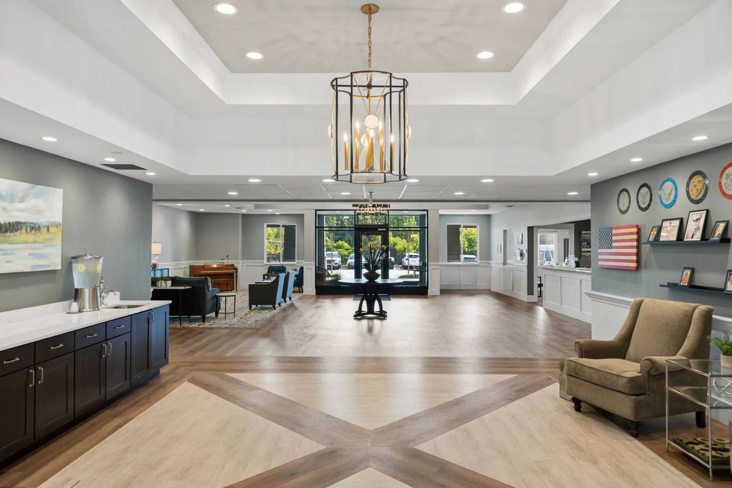 Interior view of a spacious, modern lobby with a chandelier hanging from the ceiling, comfortable chairs, tables, and decorative elements, with large windows at the back letting in natural light.