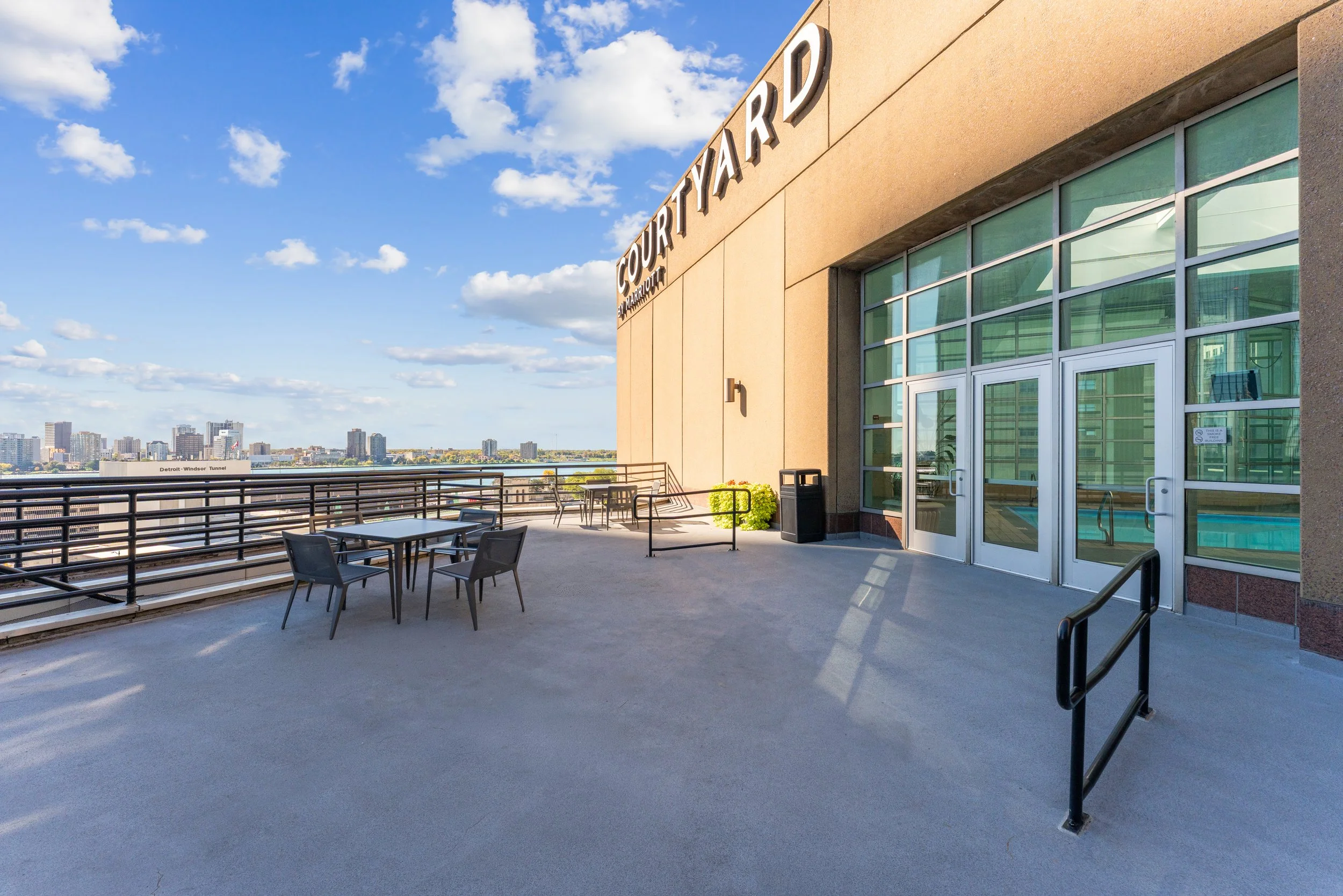 Outdoor balcony at Courtyard by Marriott featuring tables and chairs, overlooking city buildings under a clear blue sky with scattered clouds.