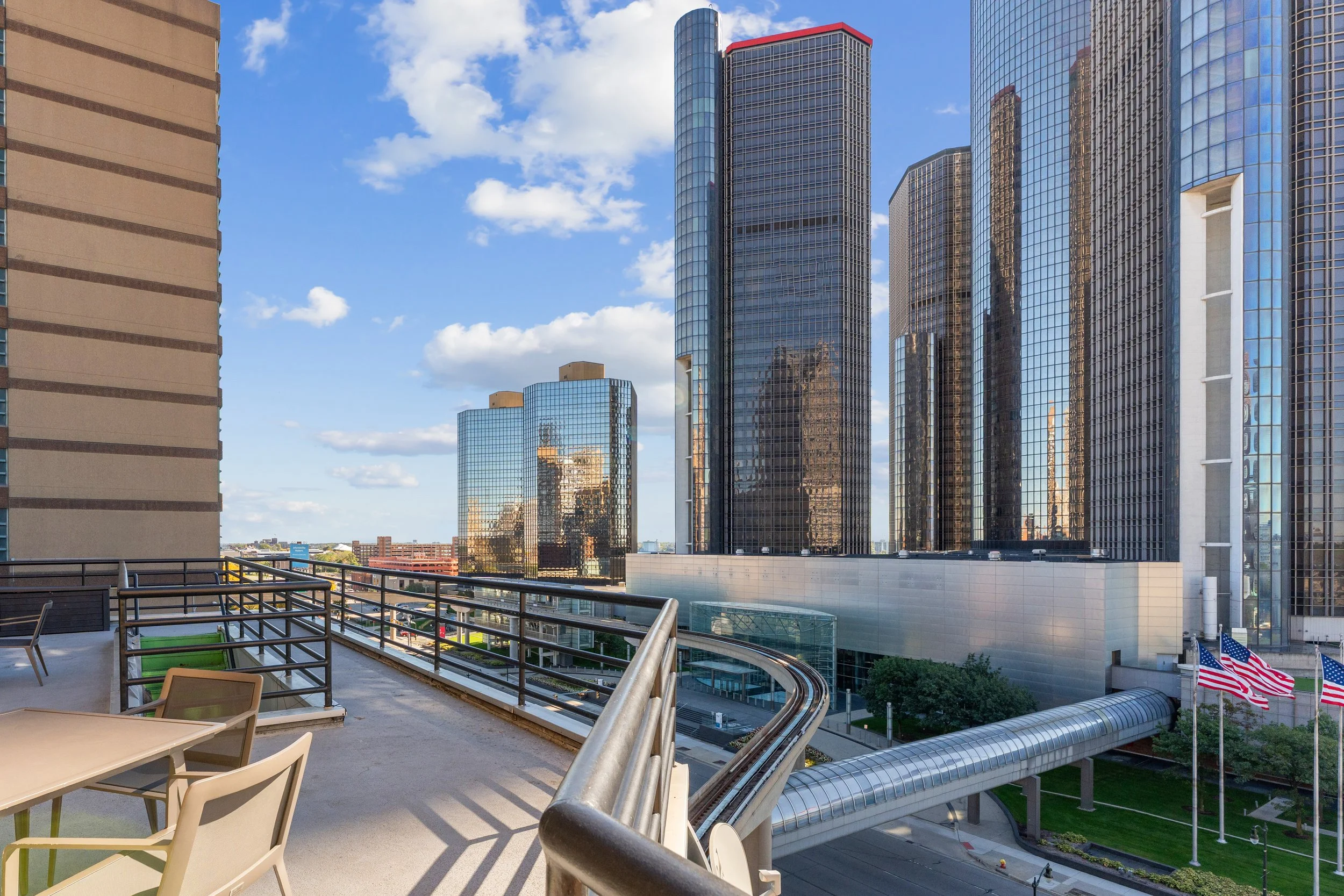 View from a balcony showing modern glass skyscrapers in a city, American flags in the lower right.
