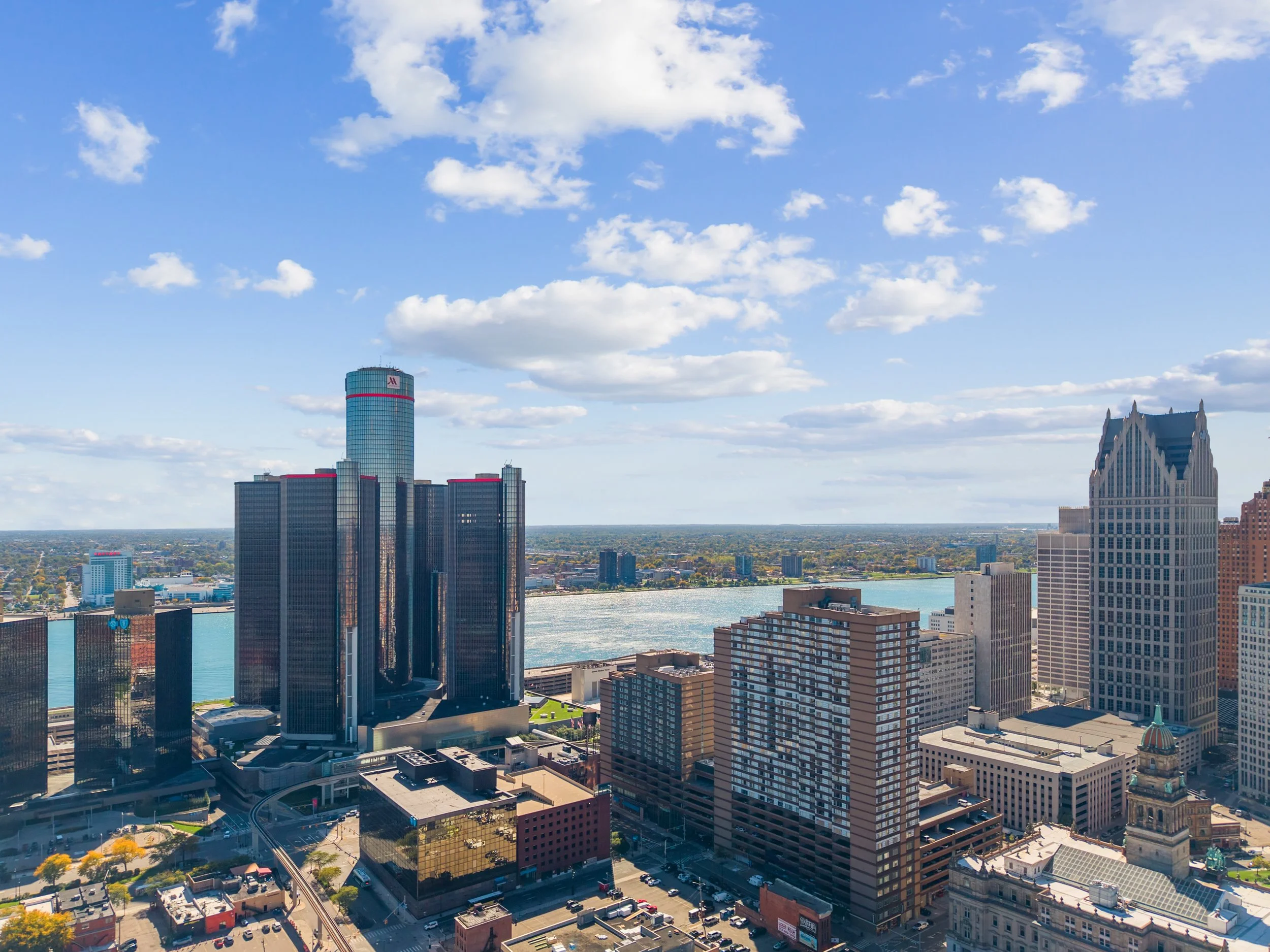 A city skyline with several tall buildings, including a glass skyscraper and a uniquely designed white building, with a river visible in the background.