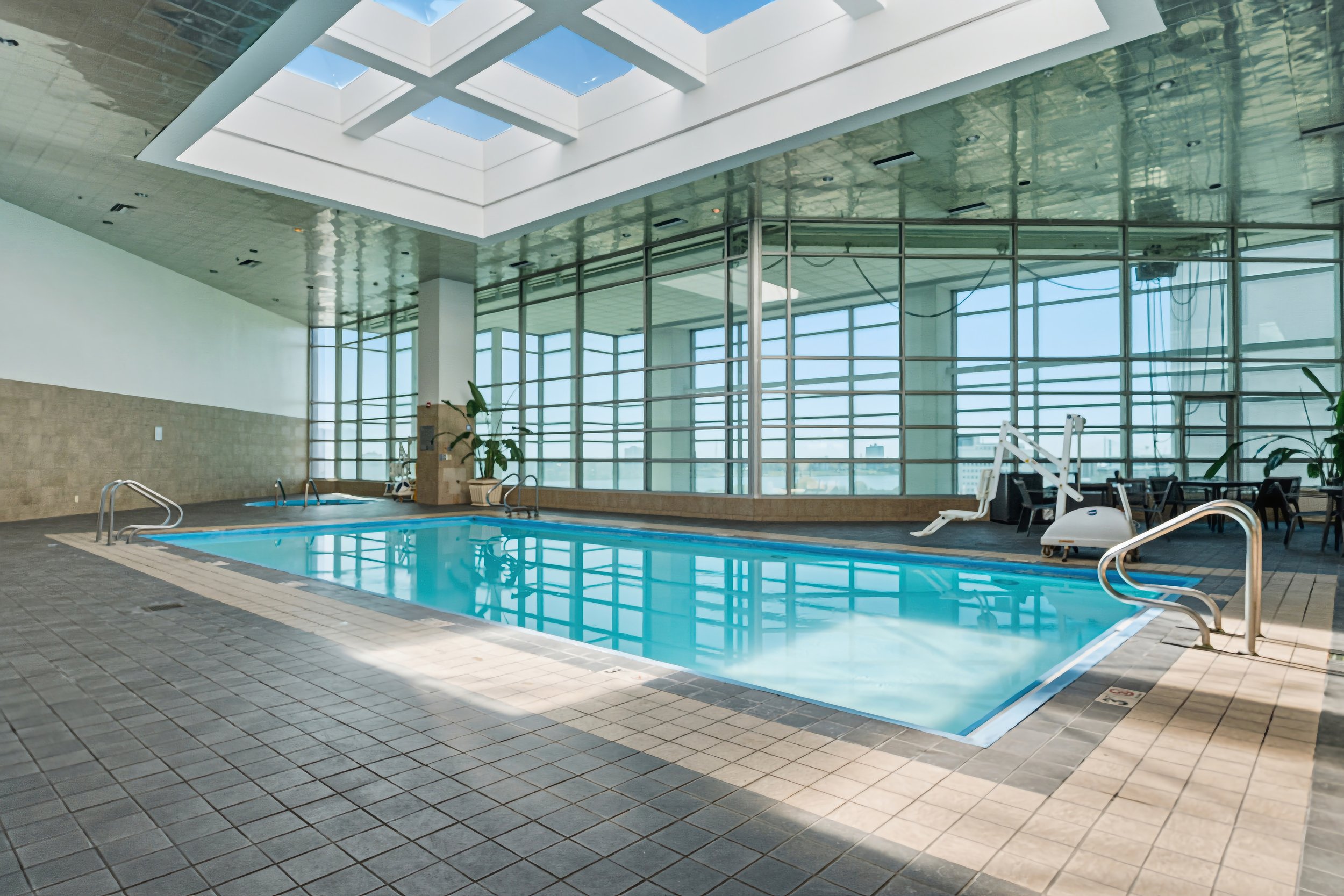 Indoor swimming pool area with large windows, skylights, lounge chairs, and exercise equipment.