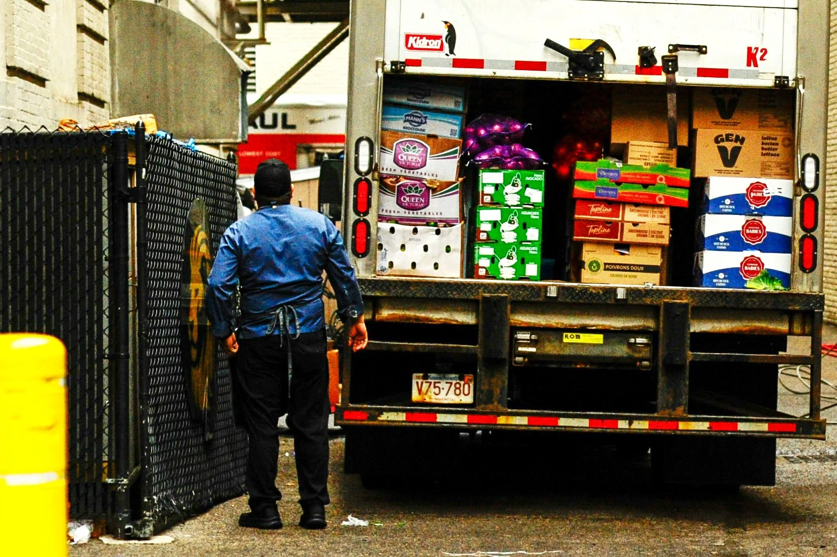 A resaurant employee meeting a delivery truck filled with boxes of produce, vegetables, and food items behind a restaurant.