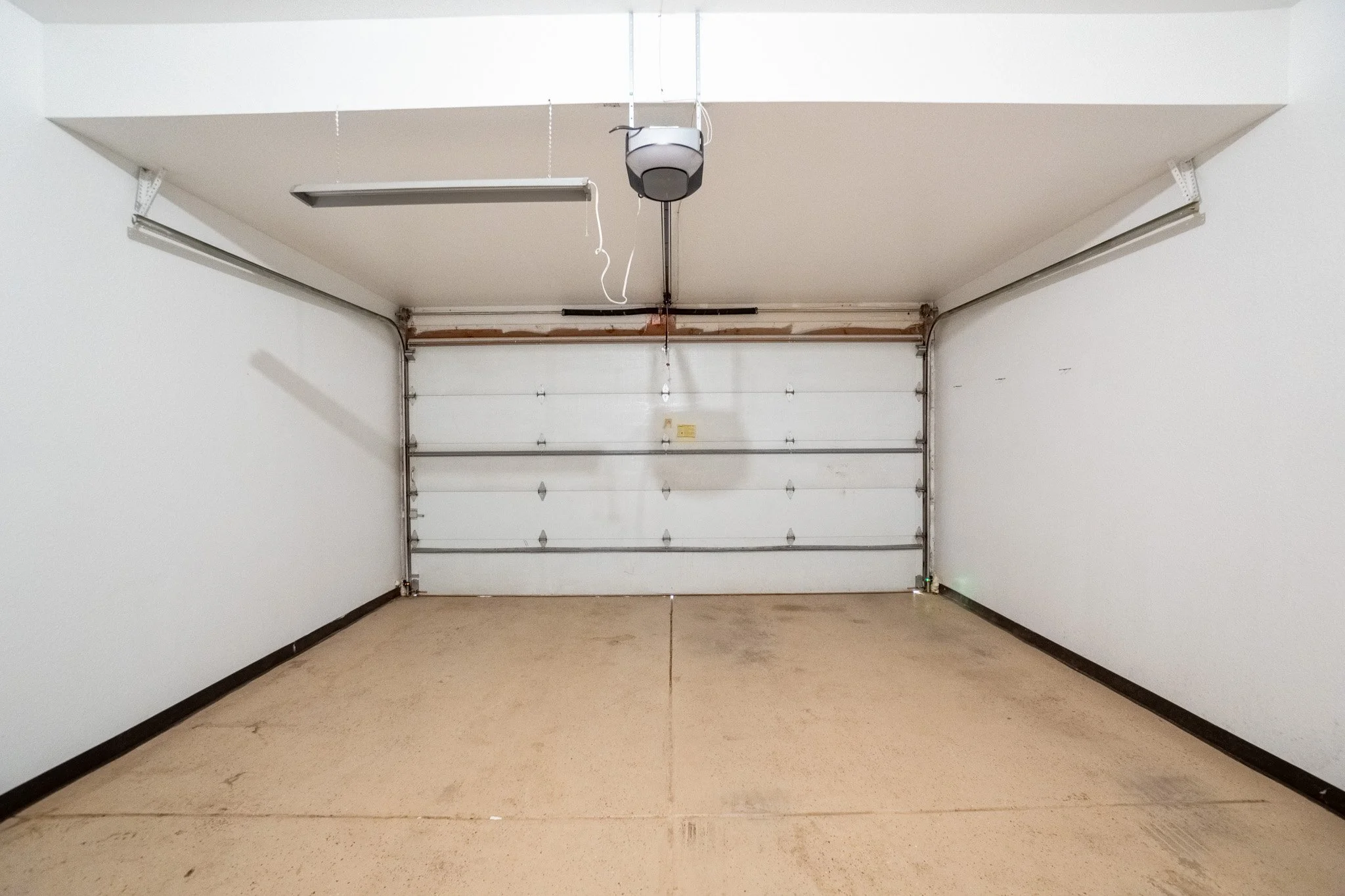 Empty garage with closed white sectional door, beige floor, white walls, and ceiling.
