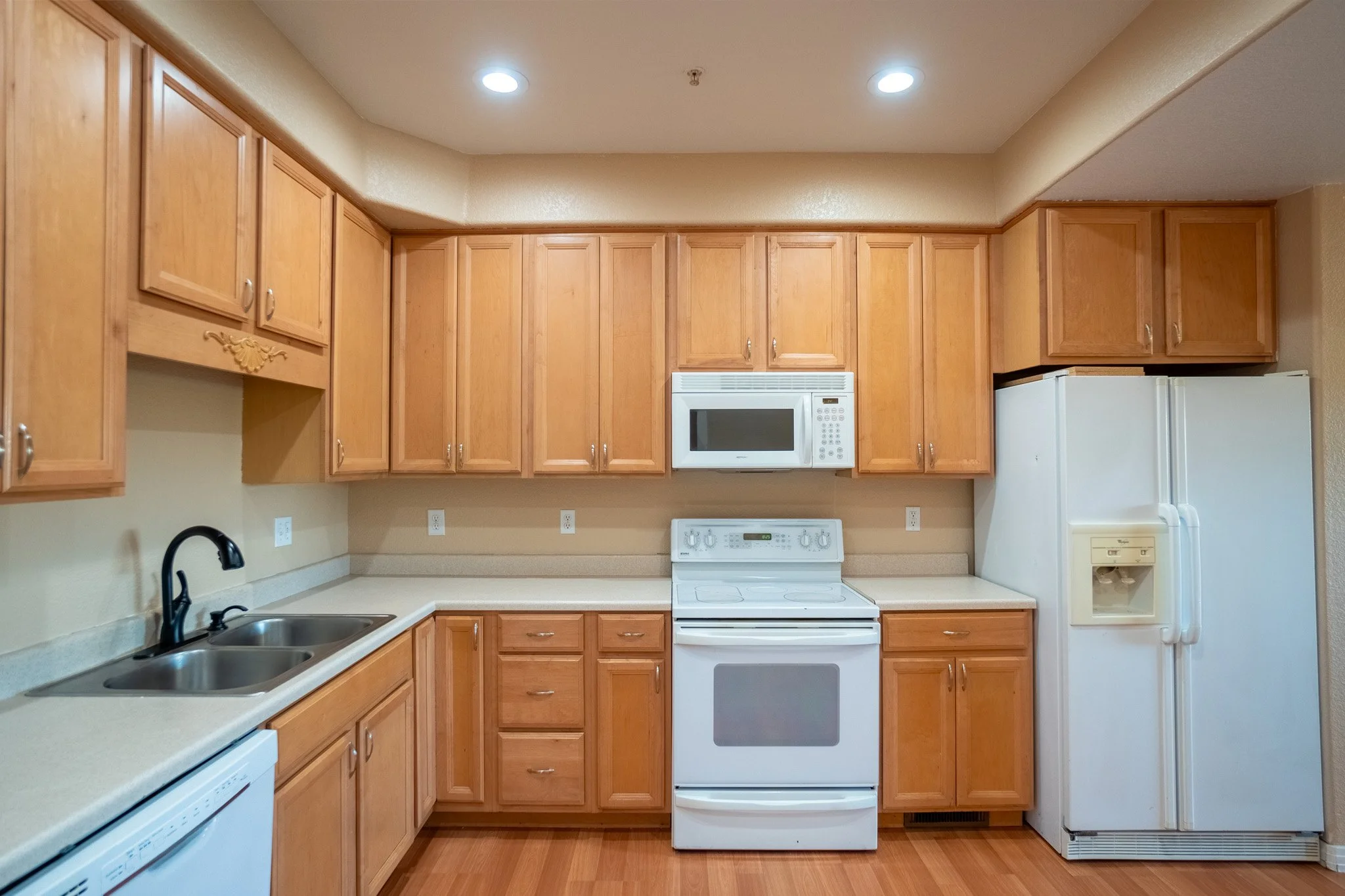 Kitchen with wooden cabinets, white appliances, a black sink faucet, and a beige countertop.