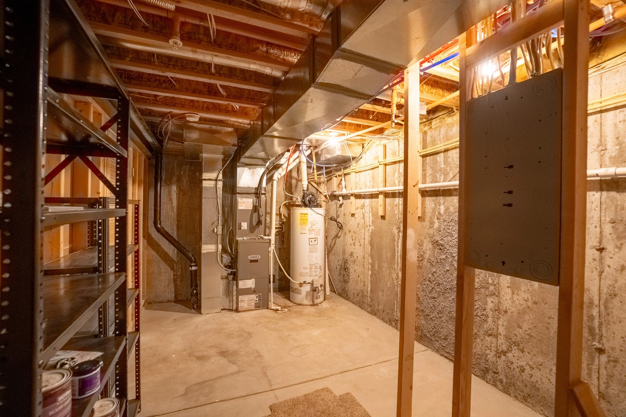 Unfinished basement with exposed wooden framing, HVAC ductwork, water heater, and utility shelving.