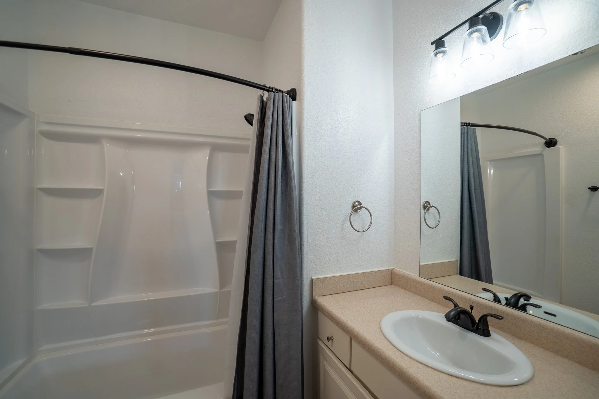 A bathroom with a shower and a mirror above a sink and countertop, with a gray shower curtain partially covering the shower.