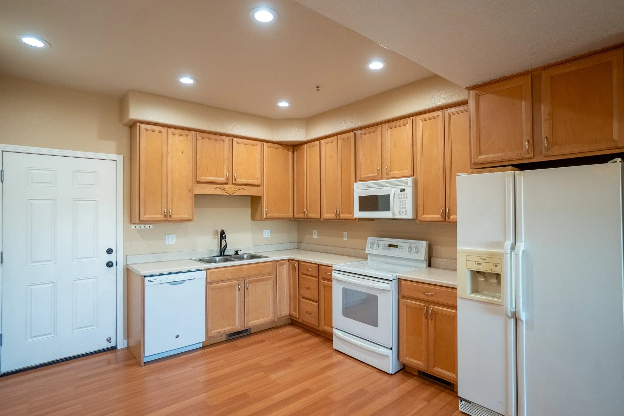 A kitchen with wooden cabinets, a white stove, microwave, dishwasher, and refrigerator, with hardwood floors and ceiling lights.