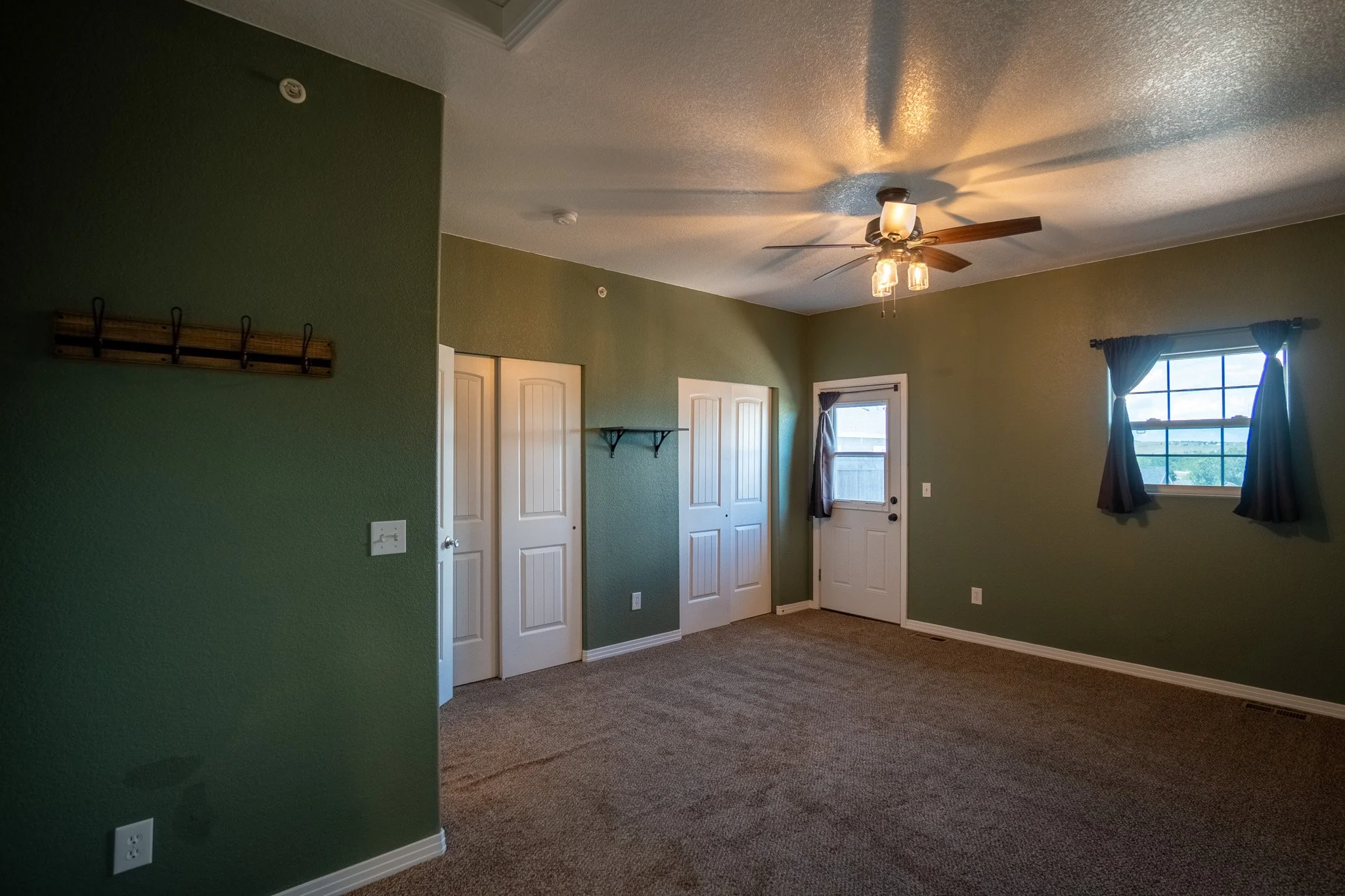 Interior view of a living room with green walls, a ceiling fan with lights, and windows with curtains.