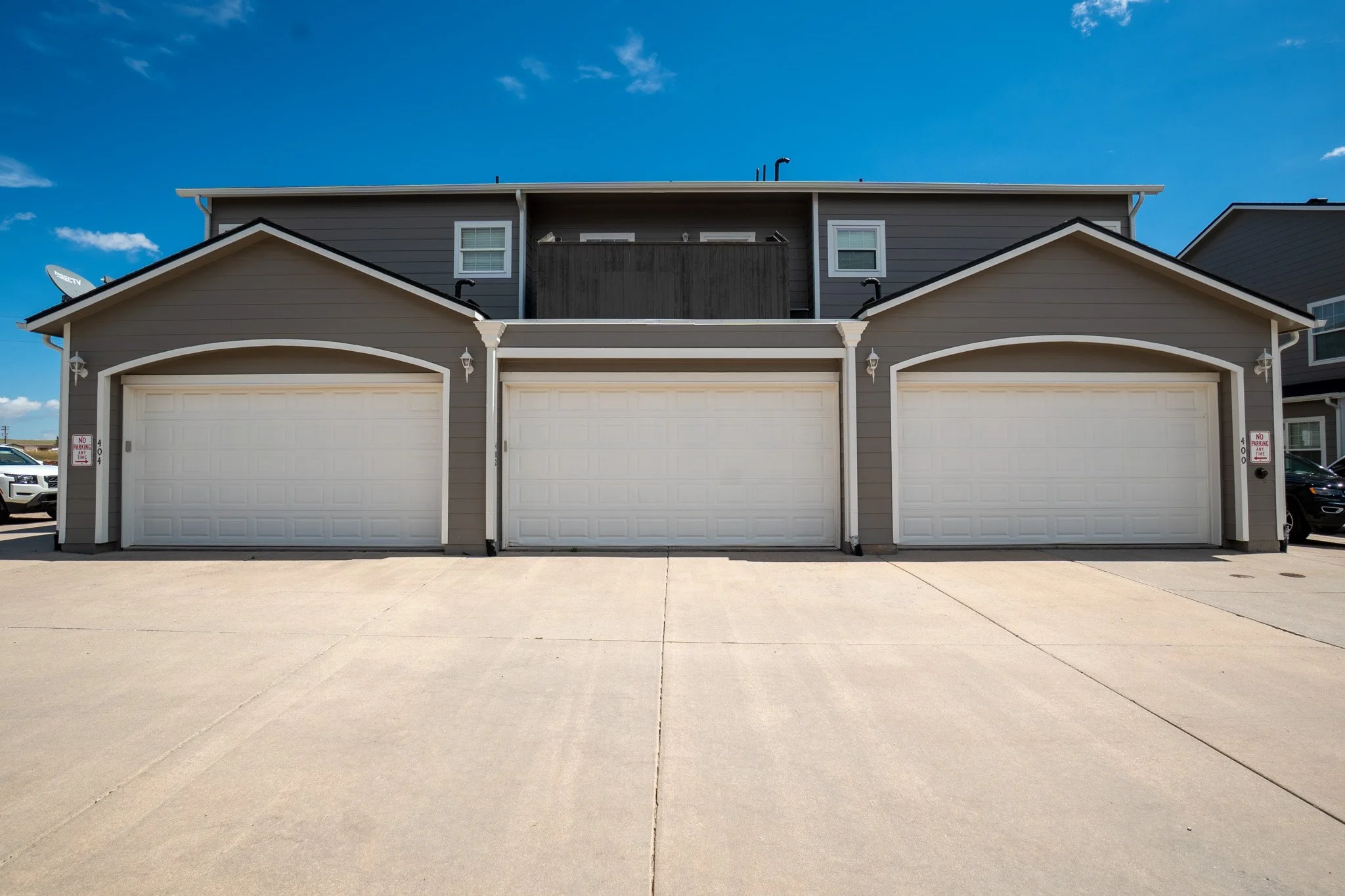 Three garages with white doors and small outdoor lights, part of a residential building, with a clear blue sky above.