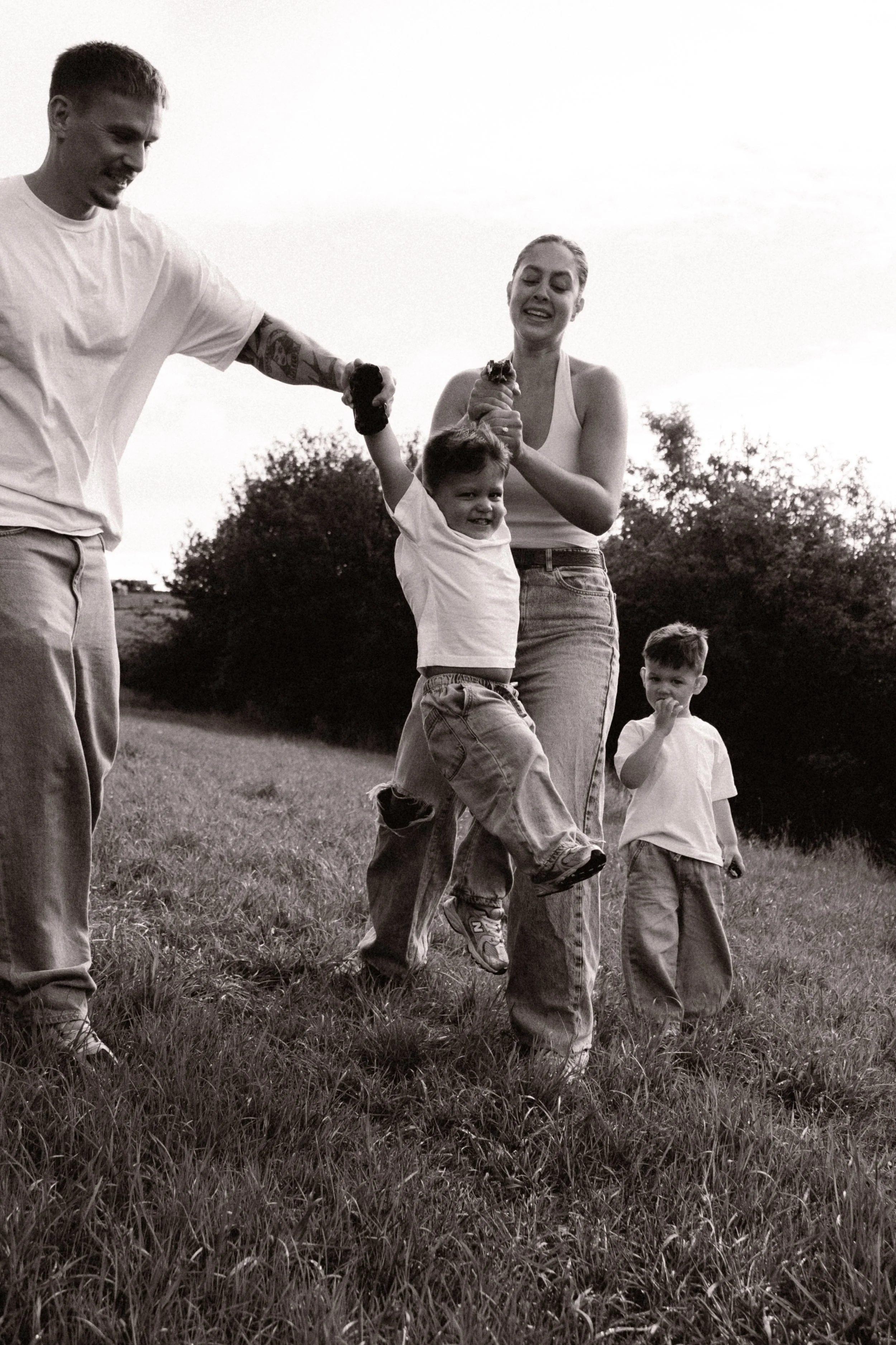 Black-and-white outdoor family scene with two adults and three children playing together in a grassy field.
