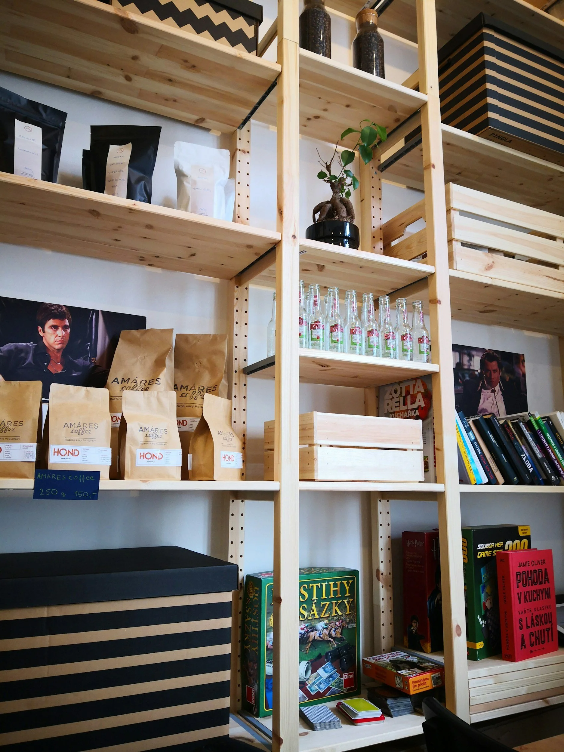 Wooden shelving unit displaying coffee bags, glass bottles, books, and board games in a cozy interior.