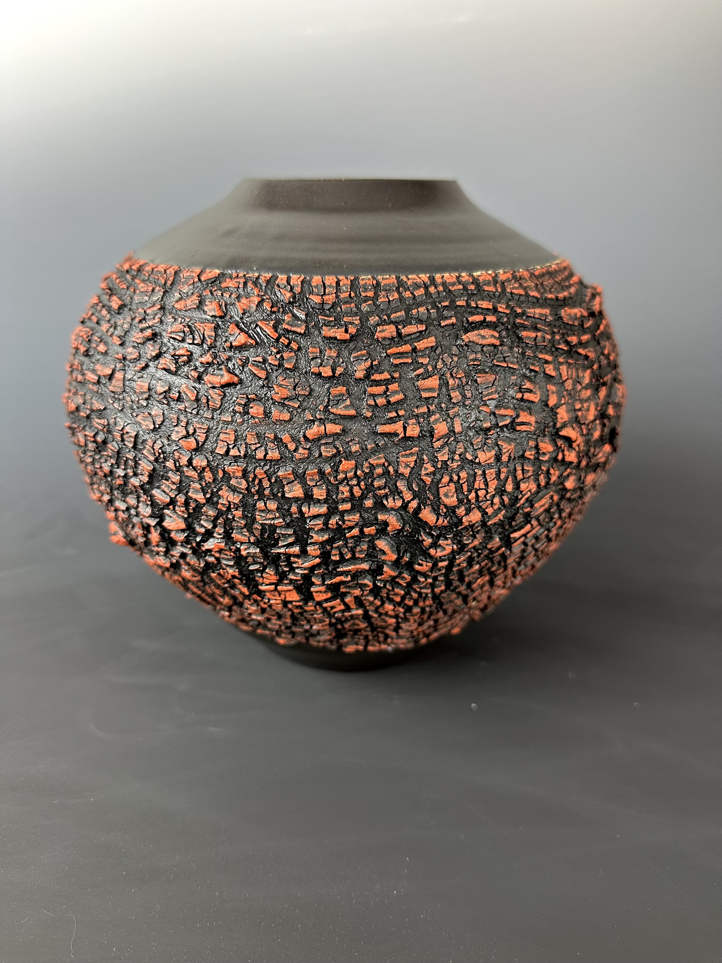 A spherical textured black and orange decorative object with a small flat top, set against a plain dark background.