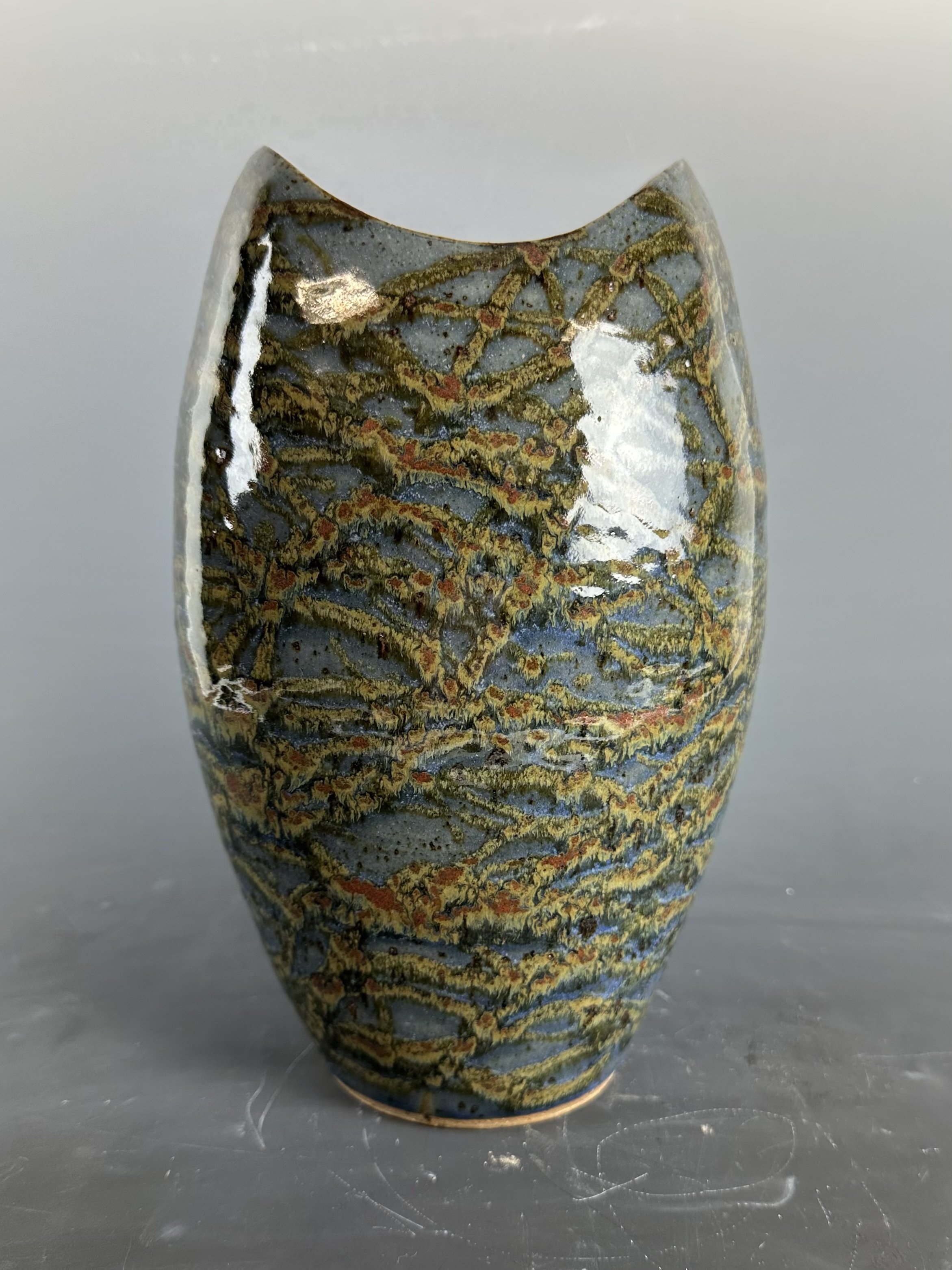 A small, painted ceramic or glass vessel with intricate, colorful swirling patterns, sitting on a reflective surface.