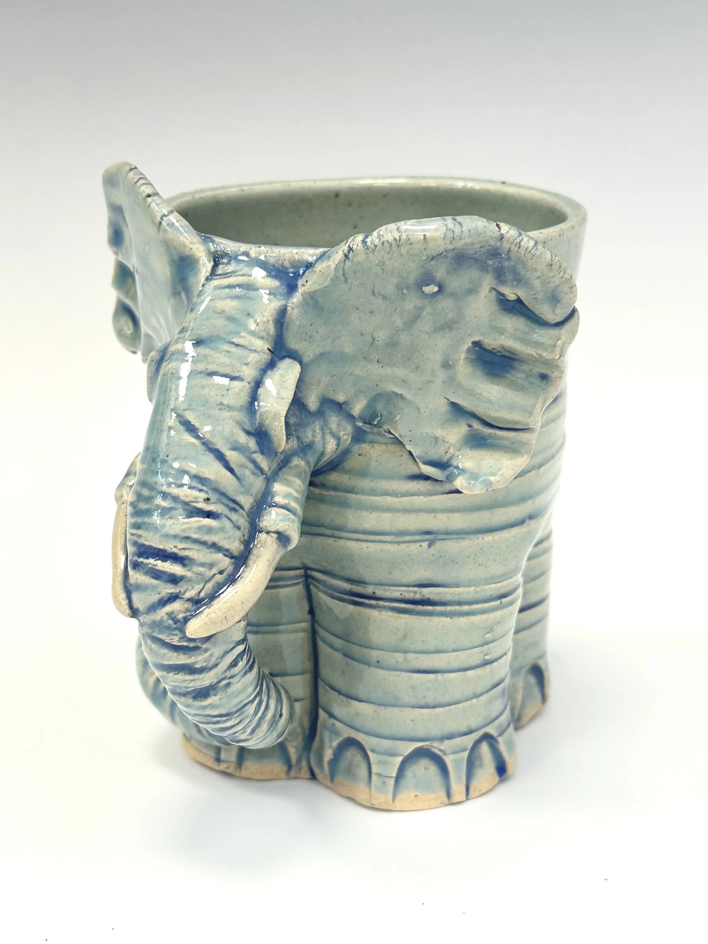 Ceramic mug designed to resemble an elephant, with textured details on the trunk and ears, glazed in shades of cream and blue.