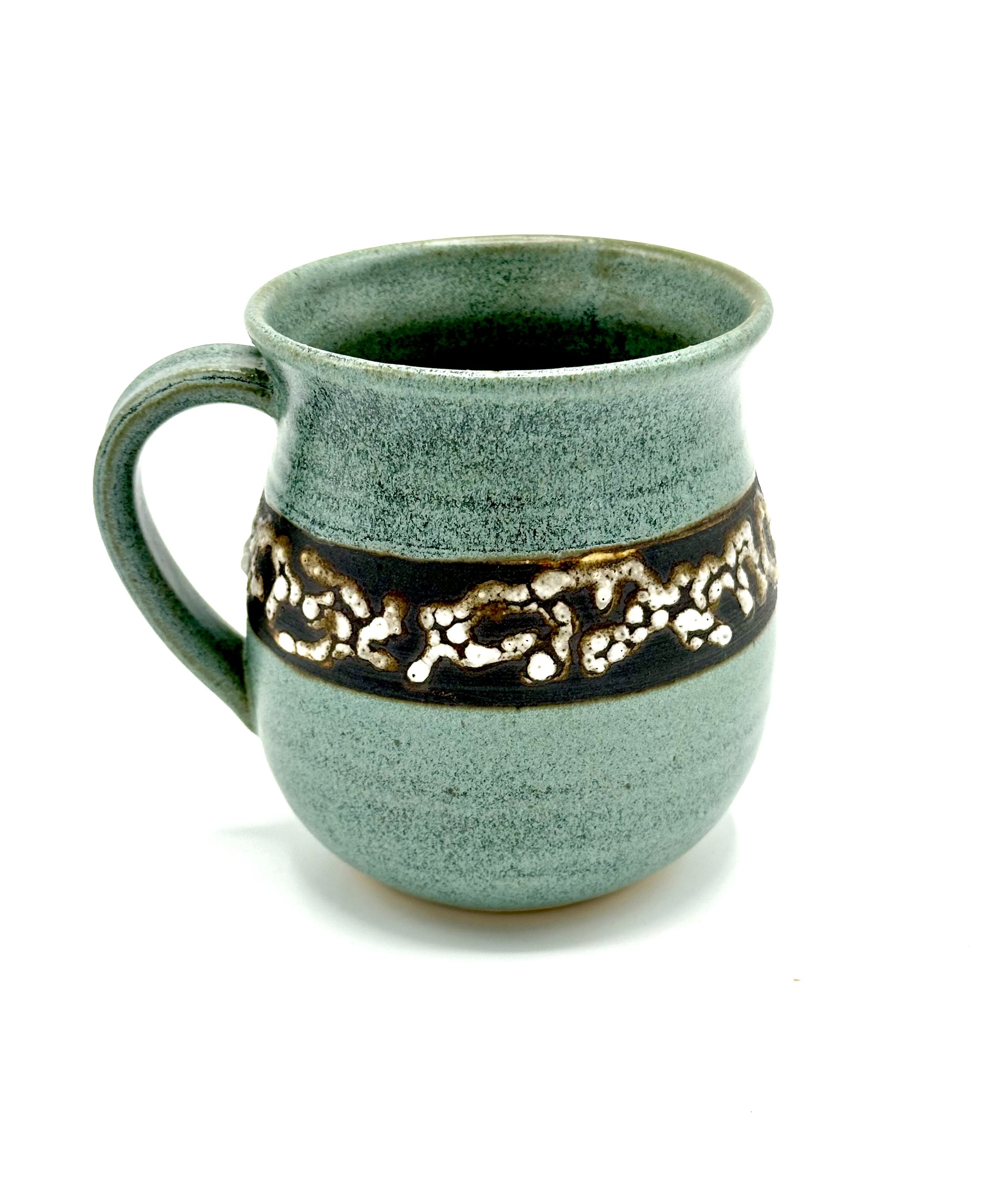 A ceramic mug with a textured, earth-tone base and a gradient green upper section, with a decorated band around its middle featuring a floral or organic design.