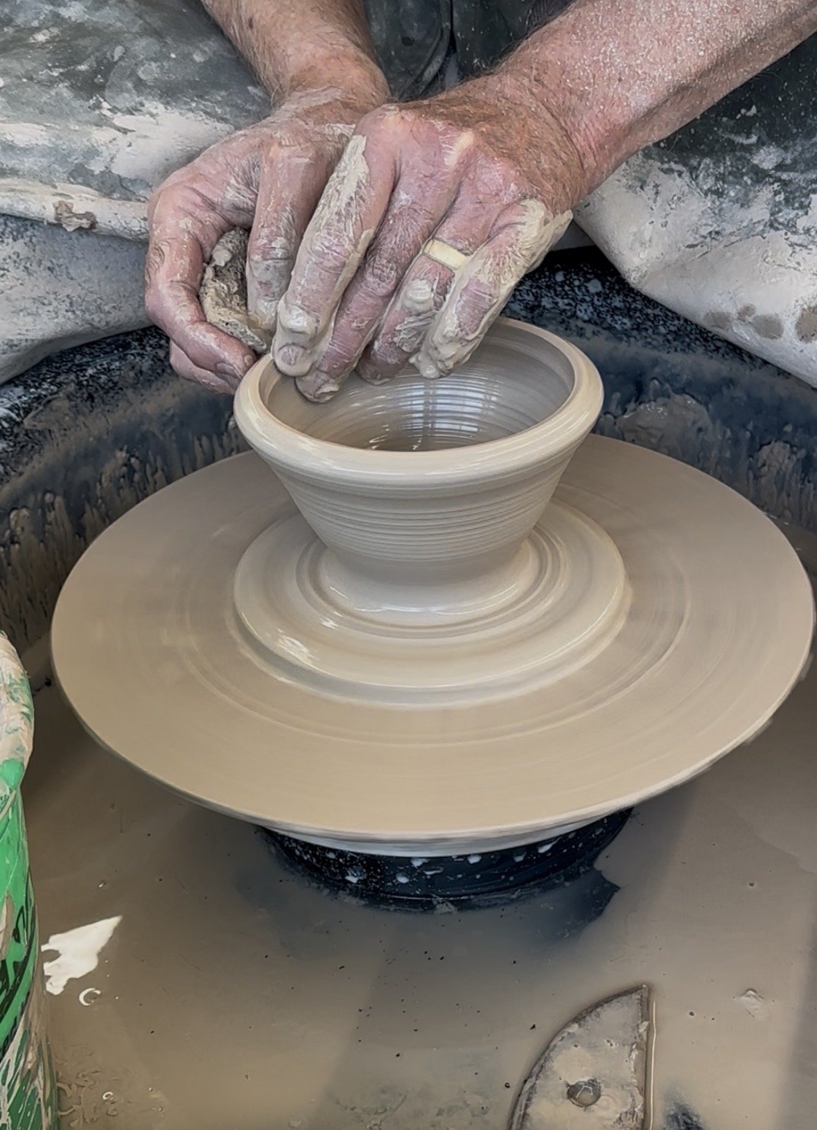 A person shaping a clay bowl on a pottery wheel, with hands covered in clay.