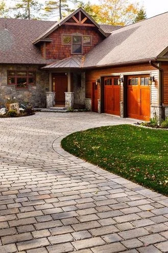Front view of a house with a stone and wood exterior, a cobblestone driveway, and a well-maintained lawn.