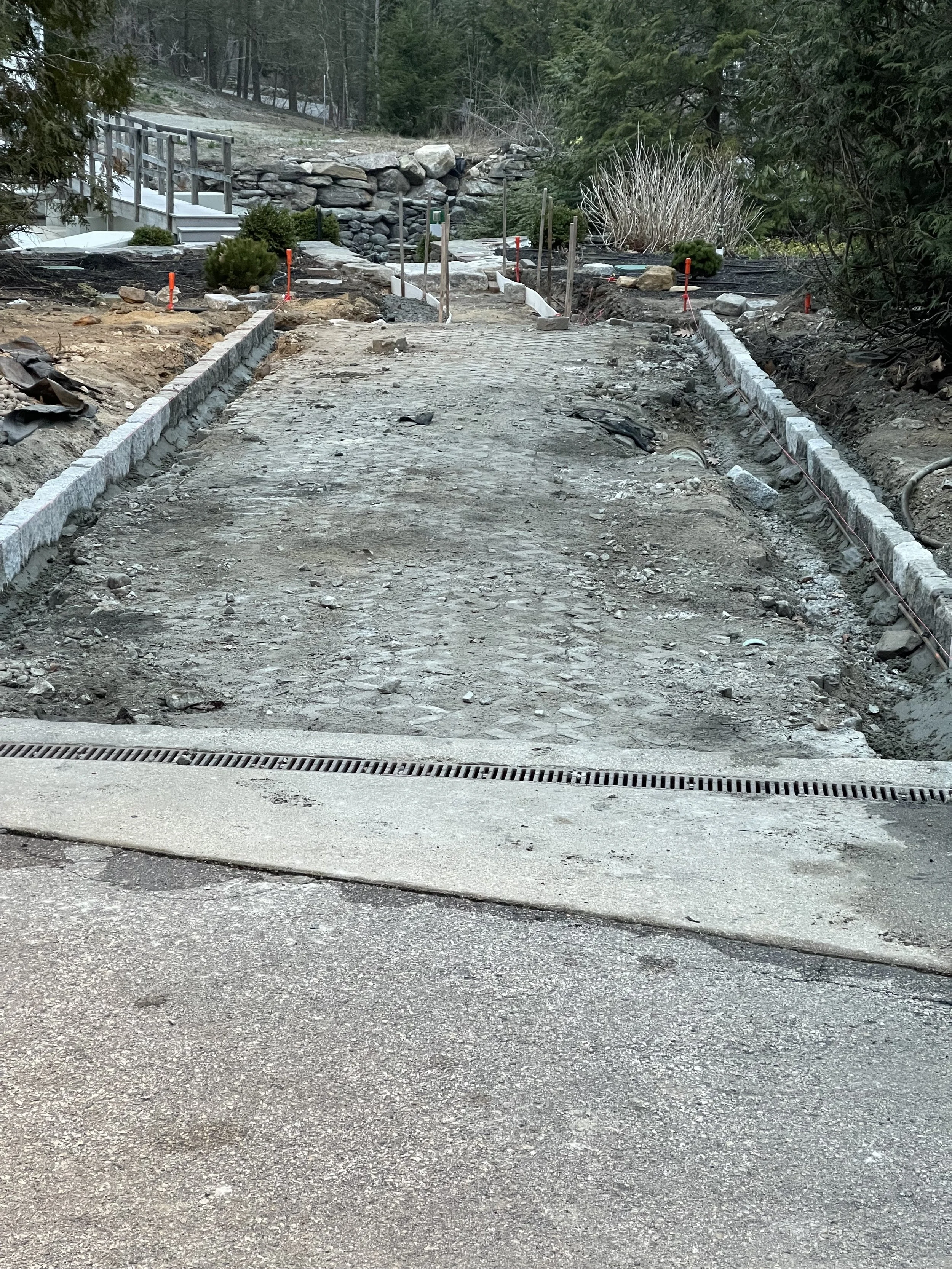 A dirt and gravel pathway under construction, with curb stones being laid on both sides, in a forested area.