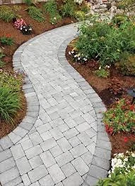 Curved paver walkway in a garden with plants and flowers on both sides