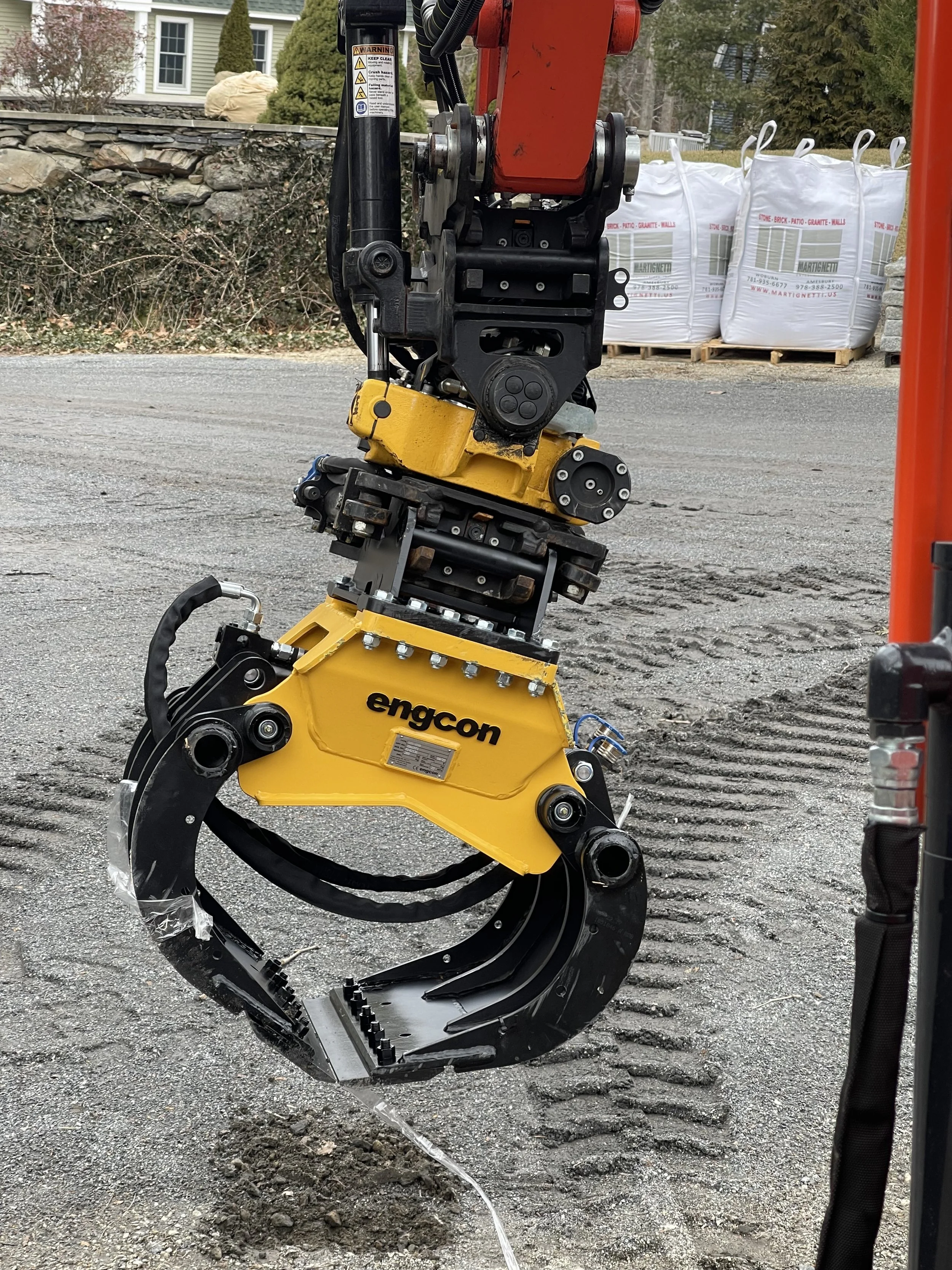 Close-up of a construction or industrial machine, specifically an attachment with hydraulic hoses and mechanical components, branded 'Engcon,' used for digging or excavating.