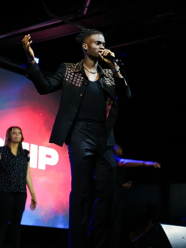 Prophet Jahhel Chosen on a worship stage, microphone in hand, arm raised