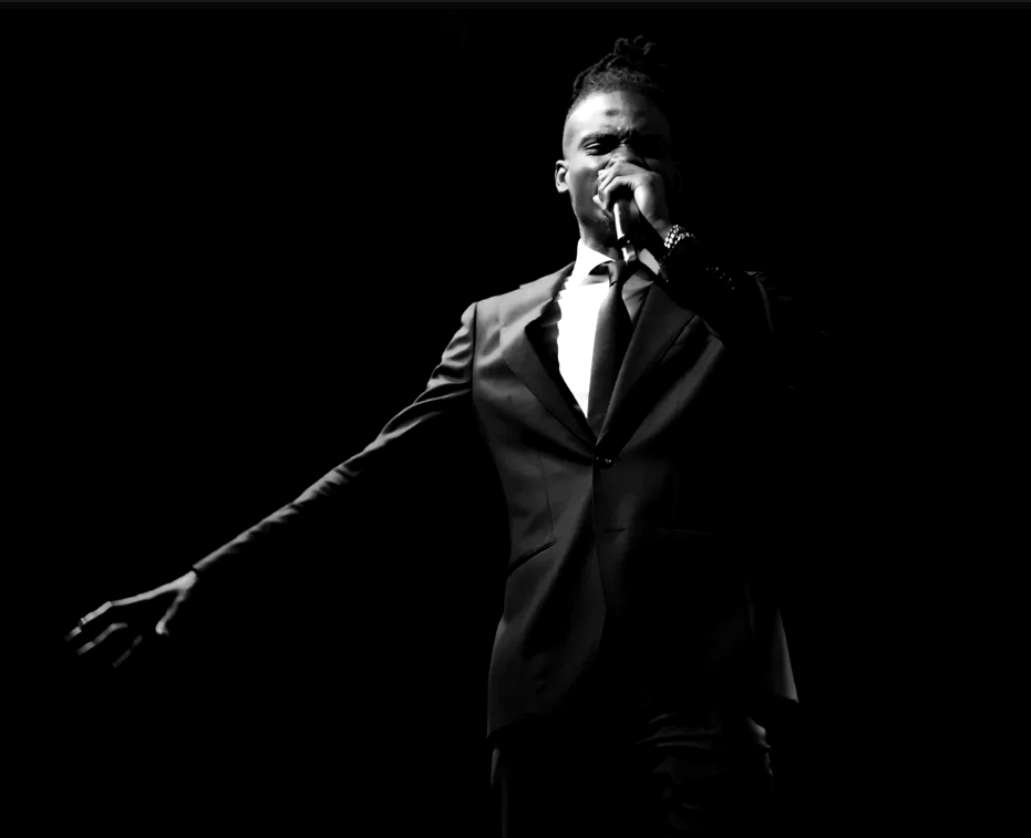 Black and white photo of Prophet Jahhel Chosen on stage, microphone raised and one arm stretched out