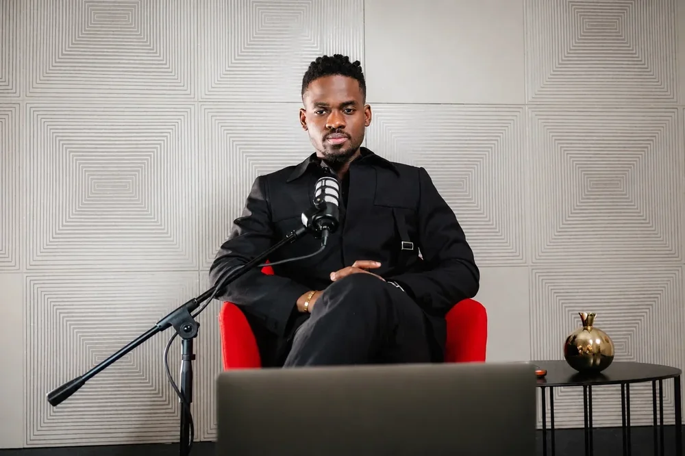 Prophet Jahhel Chosen seated in a red chair at a studio microphone, looking at the camera