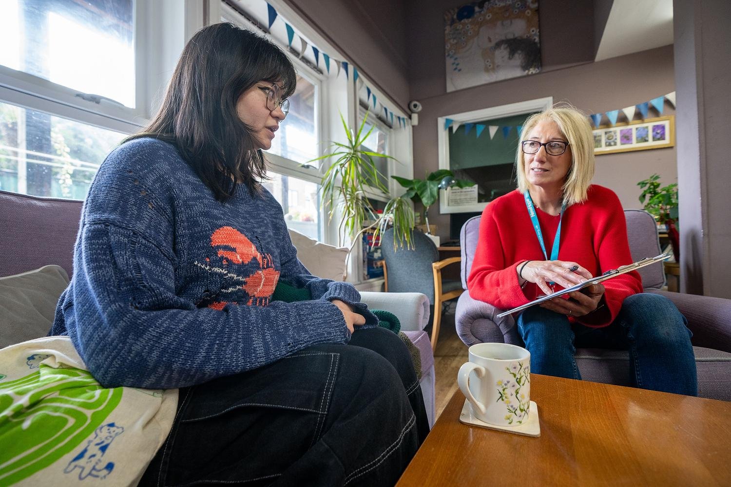 A woman in a red sweater is showing a tablet to another woman.