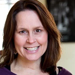 Headshot of a woman with shoulder-length brown hair, smiling with teeth showing.