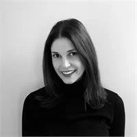 Black-and-white photo of a woman with shoulder-length hair, smiling, wearing a turtleneck sweater, against a plain background.