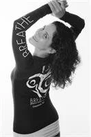 Woman with curly hair posing with her hand behind her head, wearing a black shirt with letters and a design on it