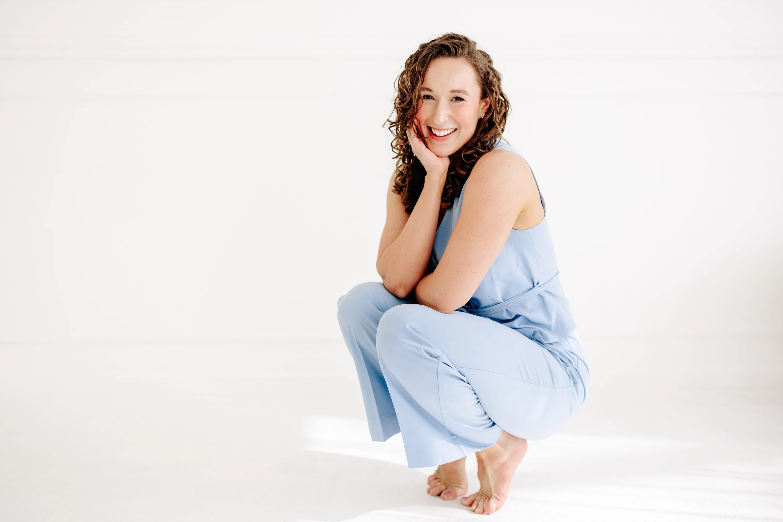 Moriah, founder of Spoonful of Blueberry, smiling while crouching in a light blue jumpsuit against a white backdrop