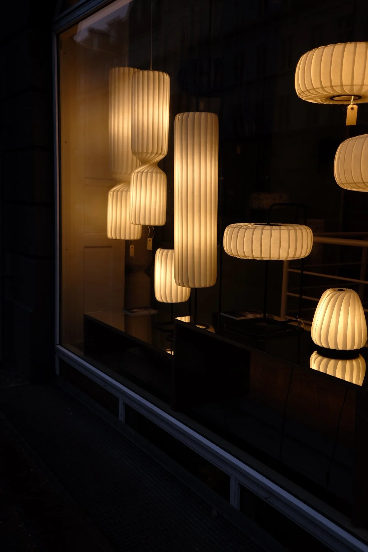 Display window with illuminated modern table lamps in various shapes and sizes, with a warm glow.