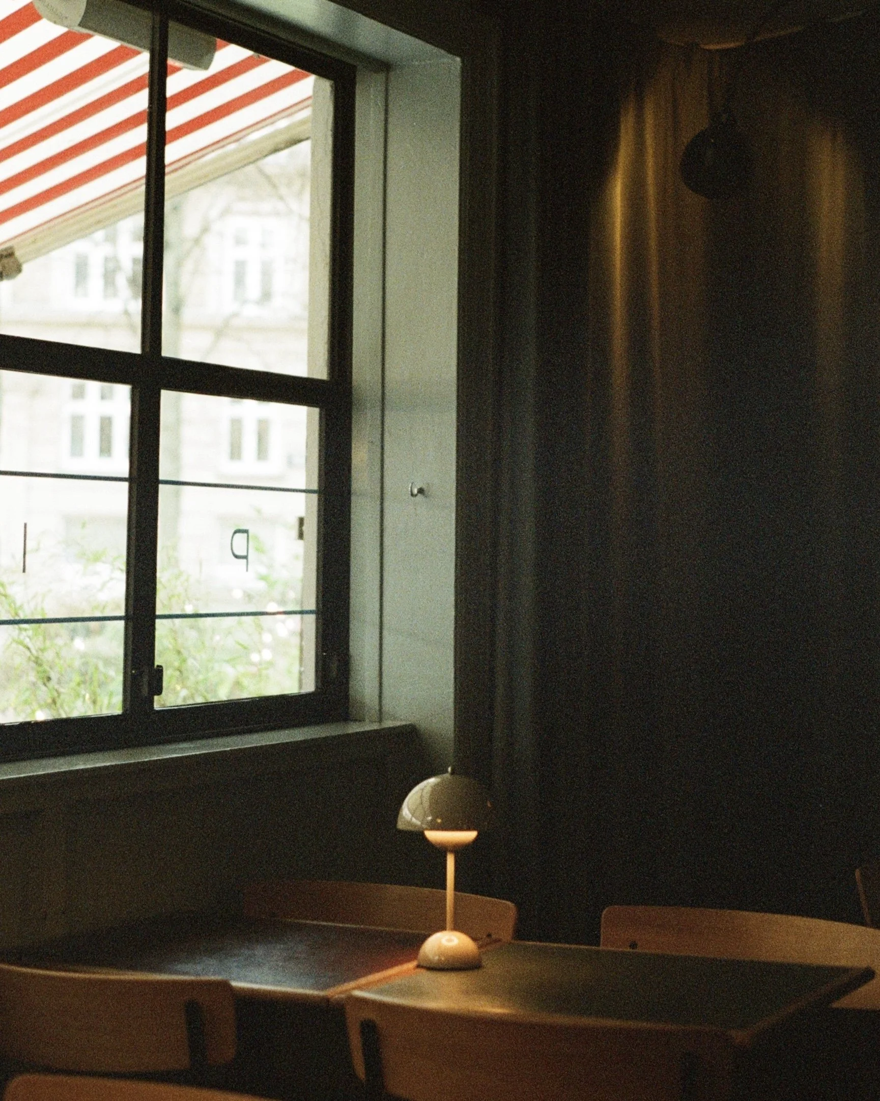 A room with a window showing an outdoor scene with buildings and trees, a dark interior with a lamp on a wooden table, and a table with a mallet and a small white ball on it.