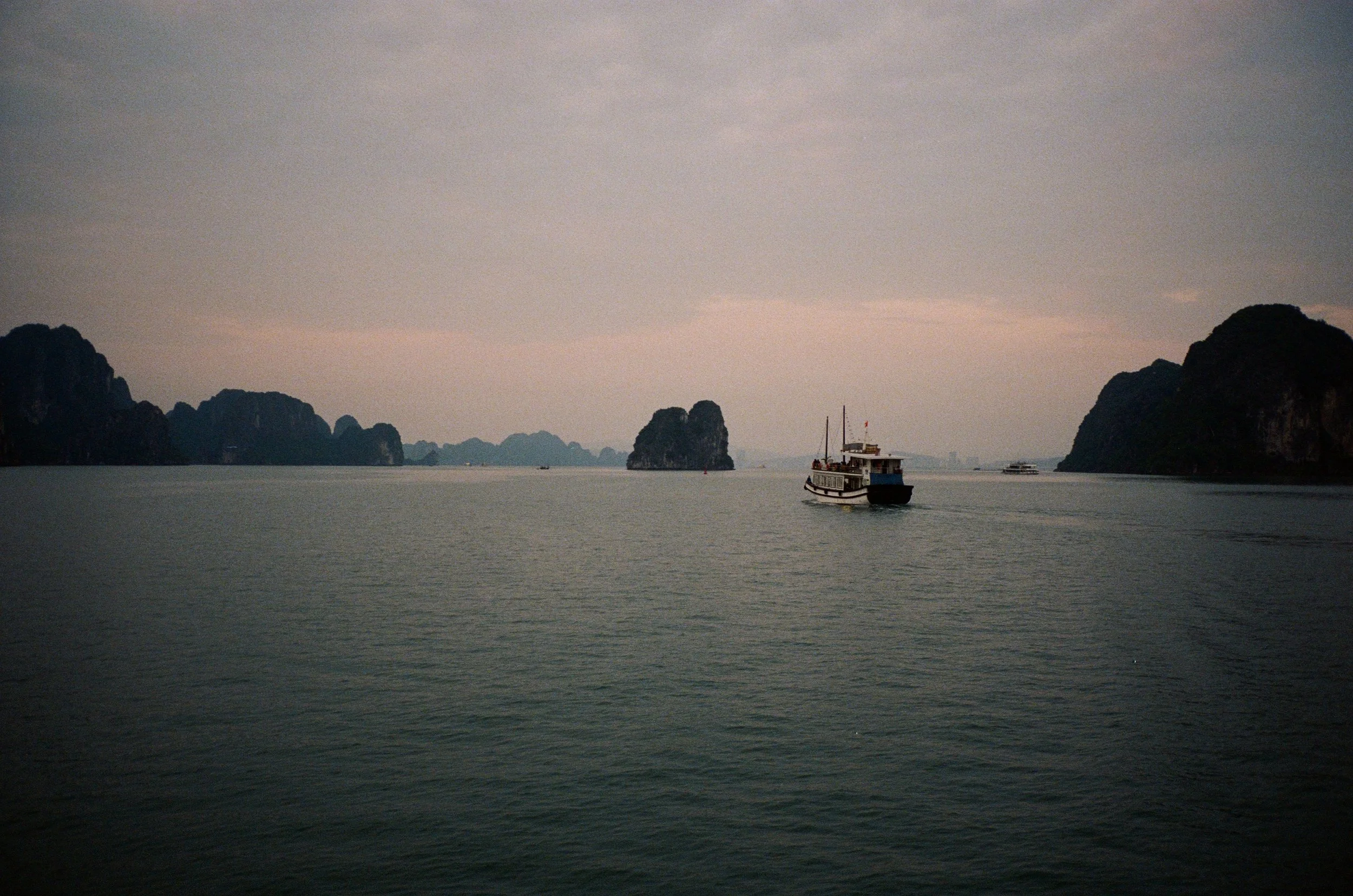 A large body of water with several small islands or limestone karsts in the background. A boat is sailing on the water near the right side of the image.