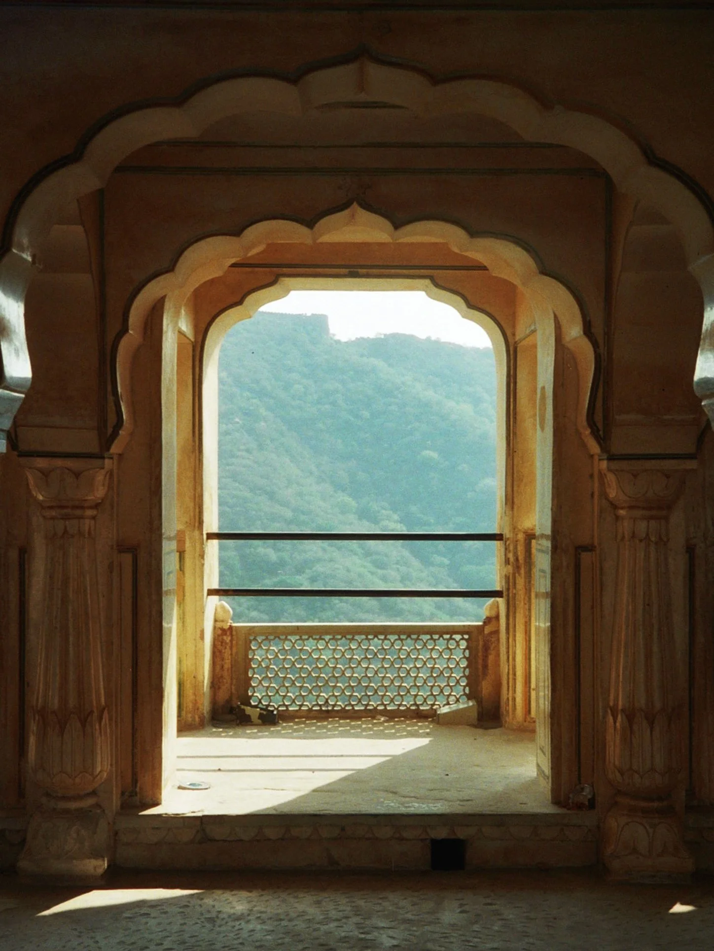 View of a traditional Indian architectural opening with intricate arches, stonework, and a scenic landscape of green hills in the background.