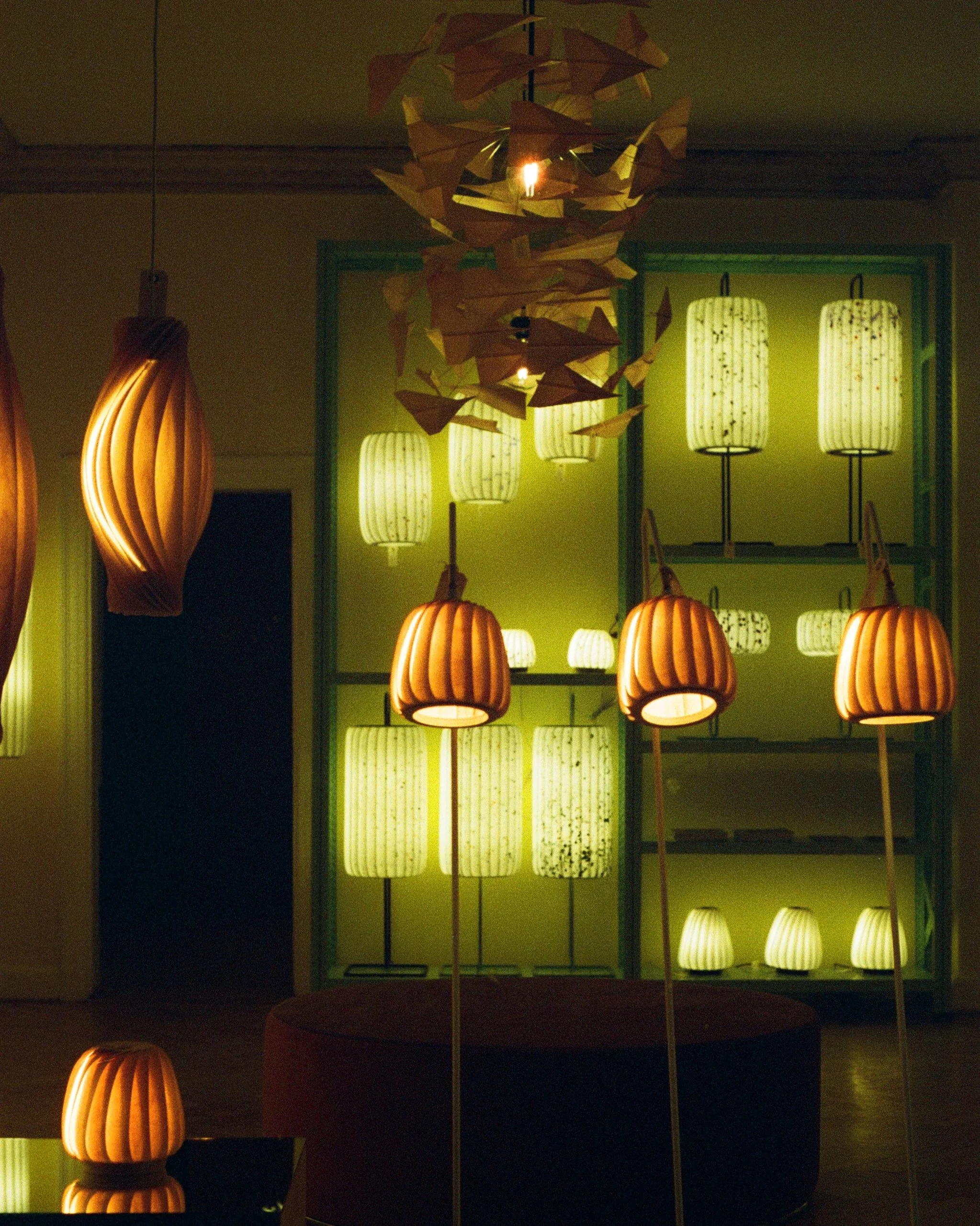A display of various illuminated paper lanterns in a dimly lit room, with a hanging paper art sculpture in the center.