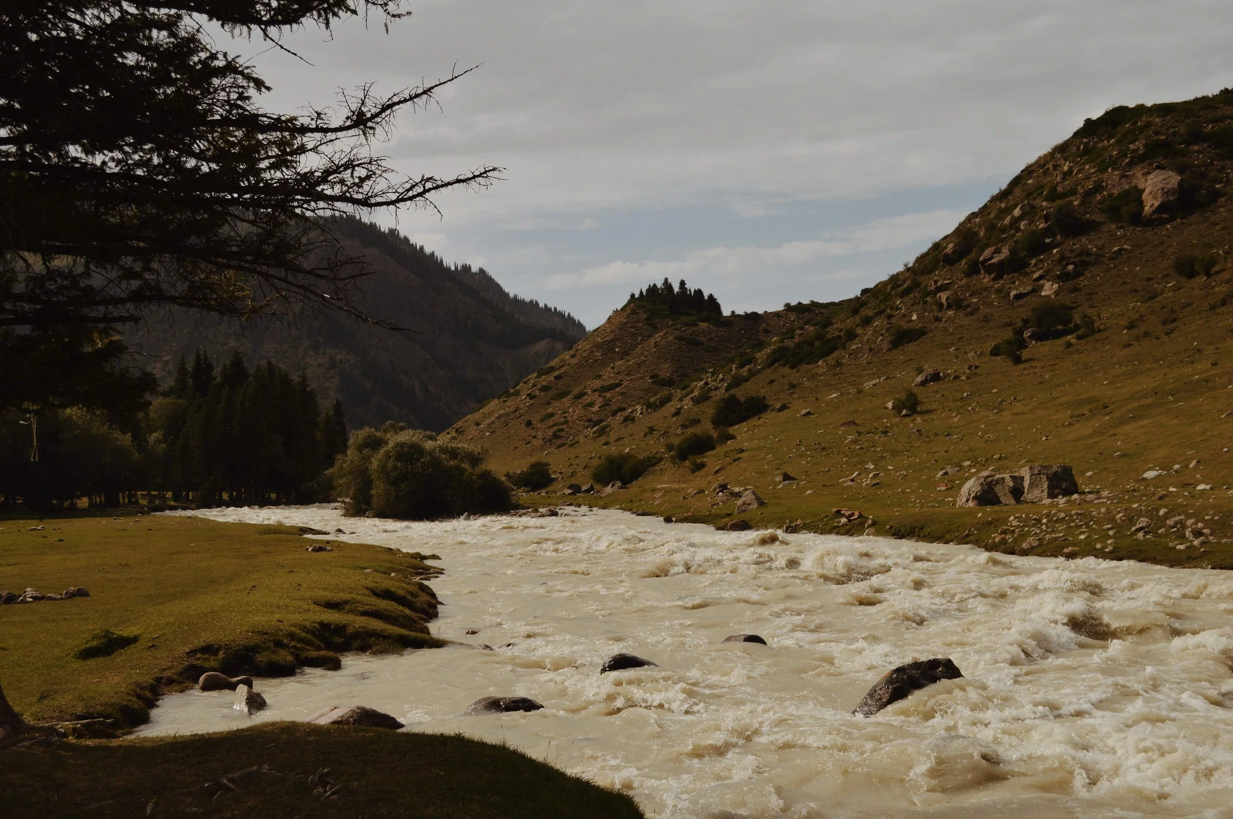 A river flowing through a valley with mountains on both sides and a cloudy sky.