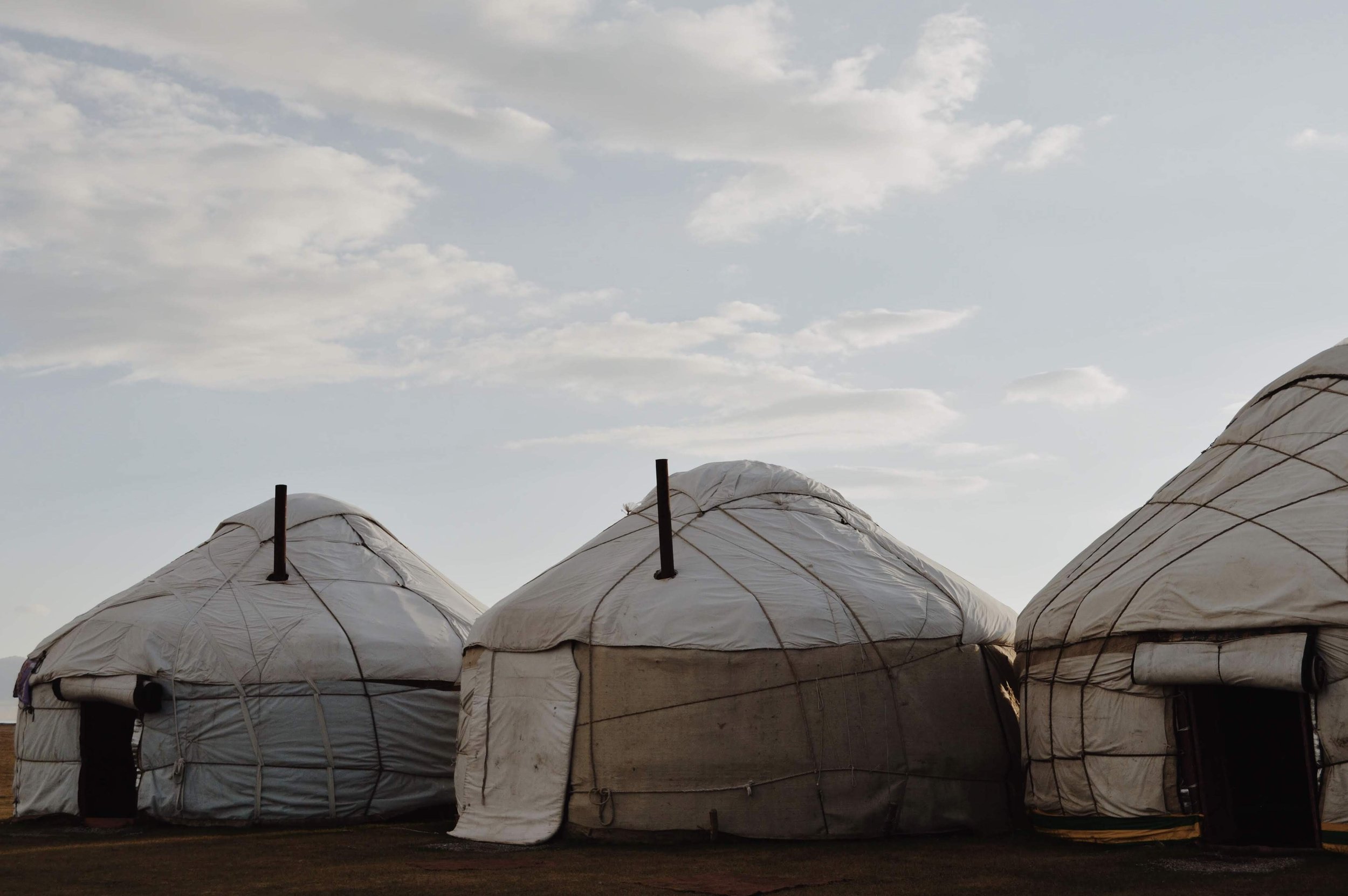 Several white, dome-shaped structures made of fabric or plastic with black poles and support wires against a sky with clouds.
