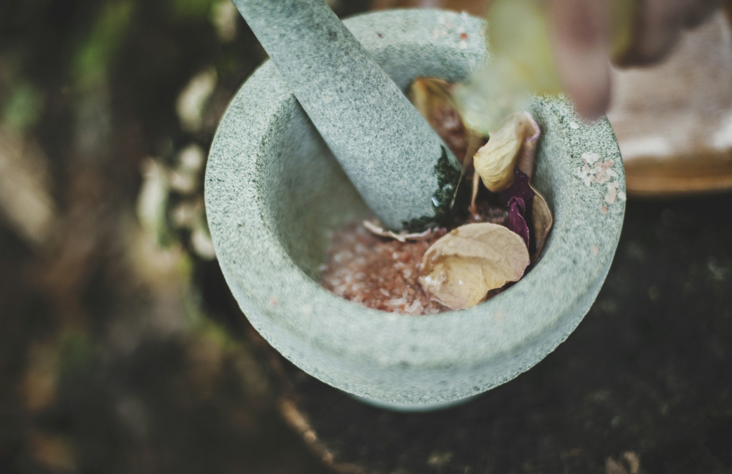 Close-up of a mortar and pestle with dried herbs or plant materials inside, used for grinding or crushing.