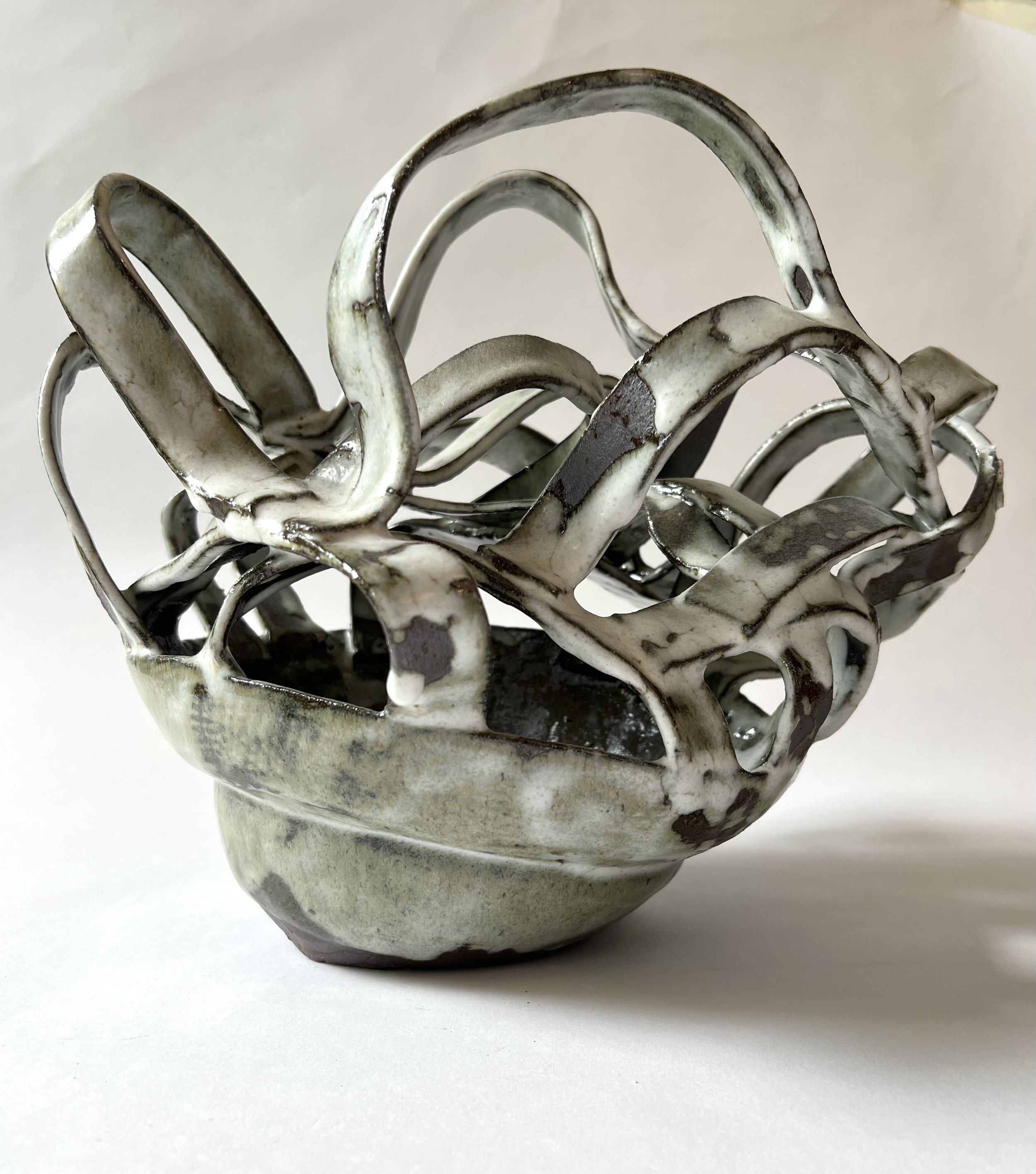 Close-up of a decorative metal basket with intertwined loops, featuring a white and black distressed glaze finish, set against a plain white background.