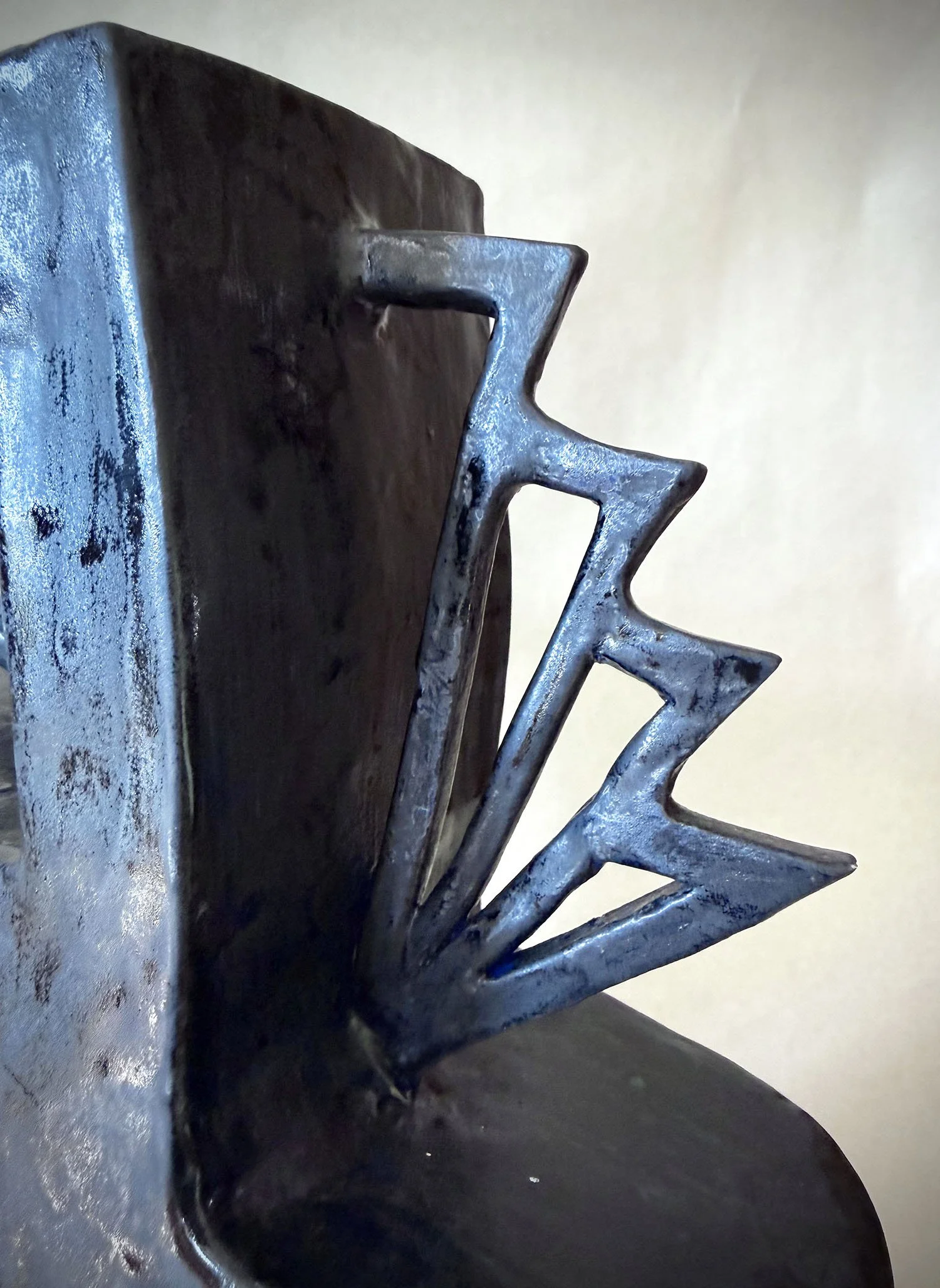 Close-up of a metal meat tenderizer with a textured, flat surface and a handle, placed on a dark surface with a plain wall in the background.