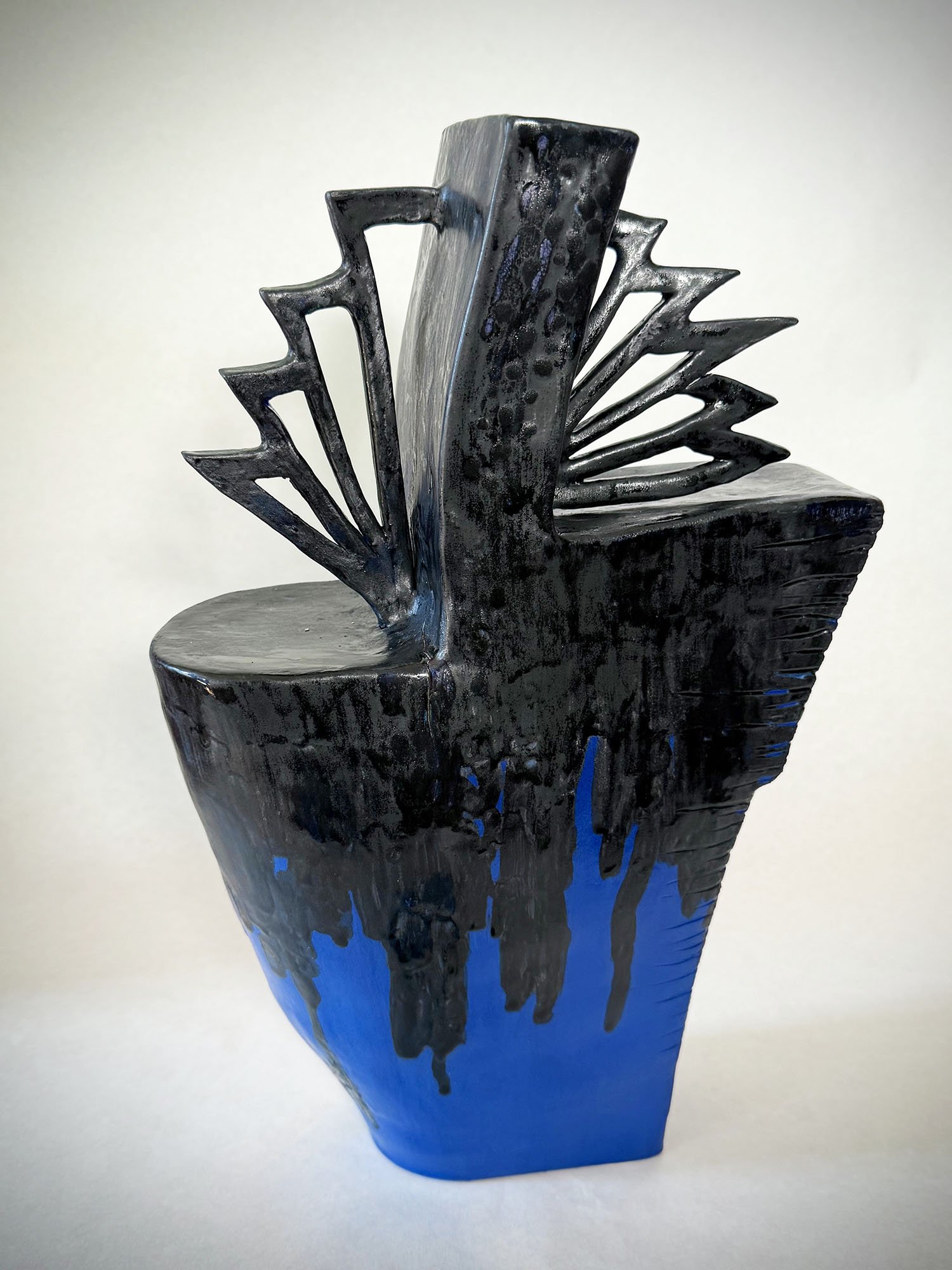 A ceramic sculpture of a chair with a black backrest and a blue base, featuring abstract, jagged protrusions extending from the backrest.