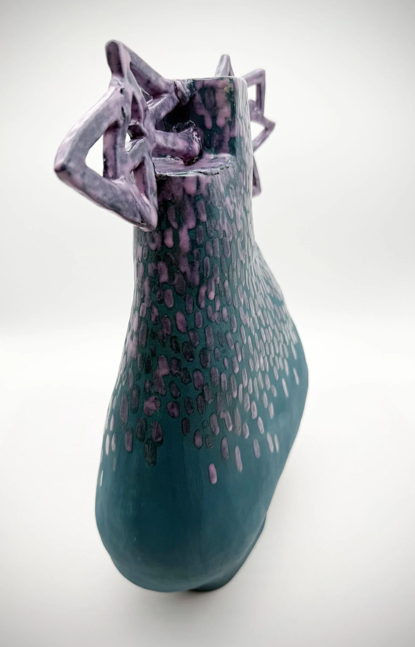 Close-up of a ceramic sculpture of a stylized animal with purple and teal patterns, set against a plain white background.