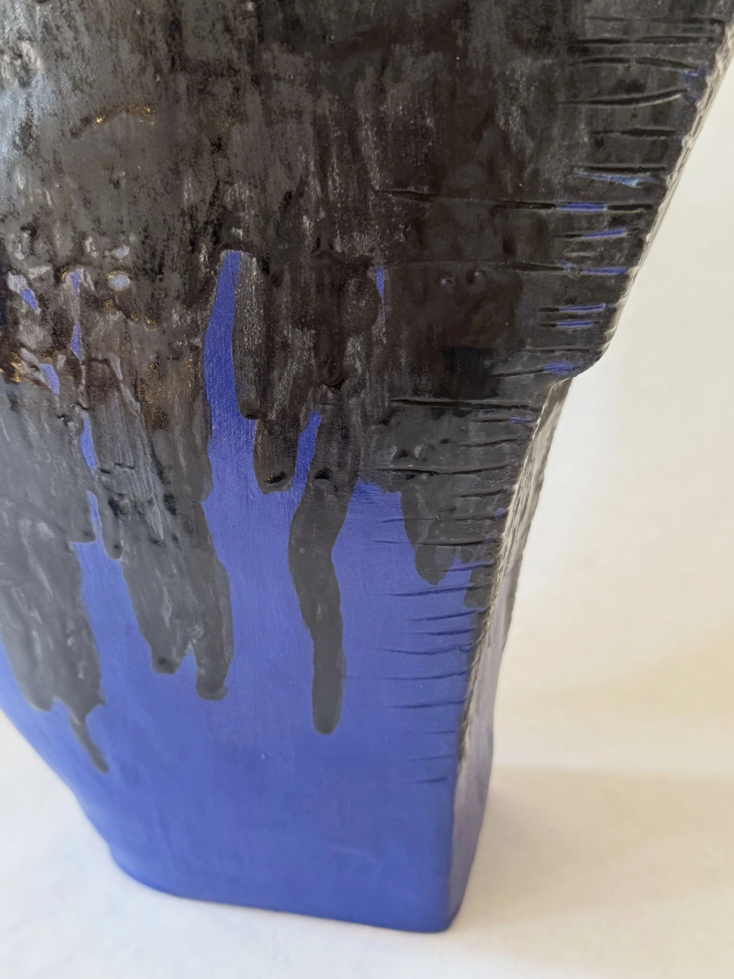 Close-up of a blue plastic object with black paint or substance dripping down its side.