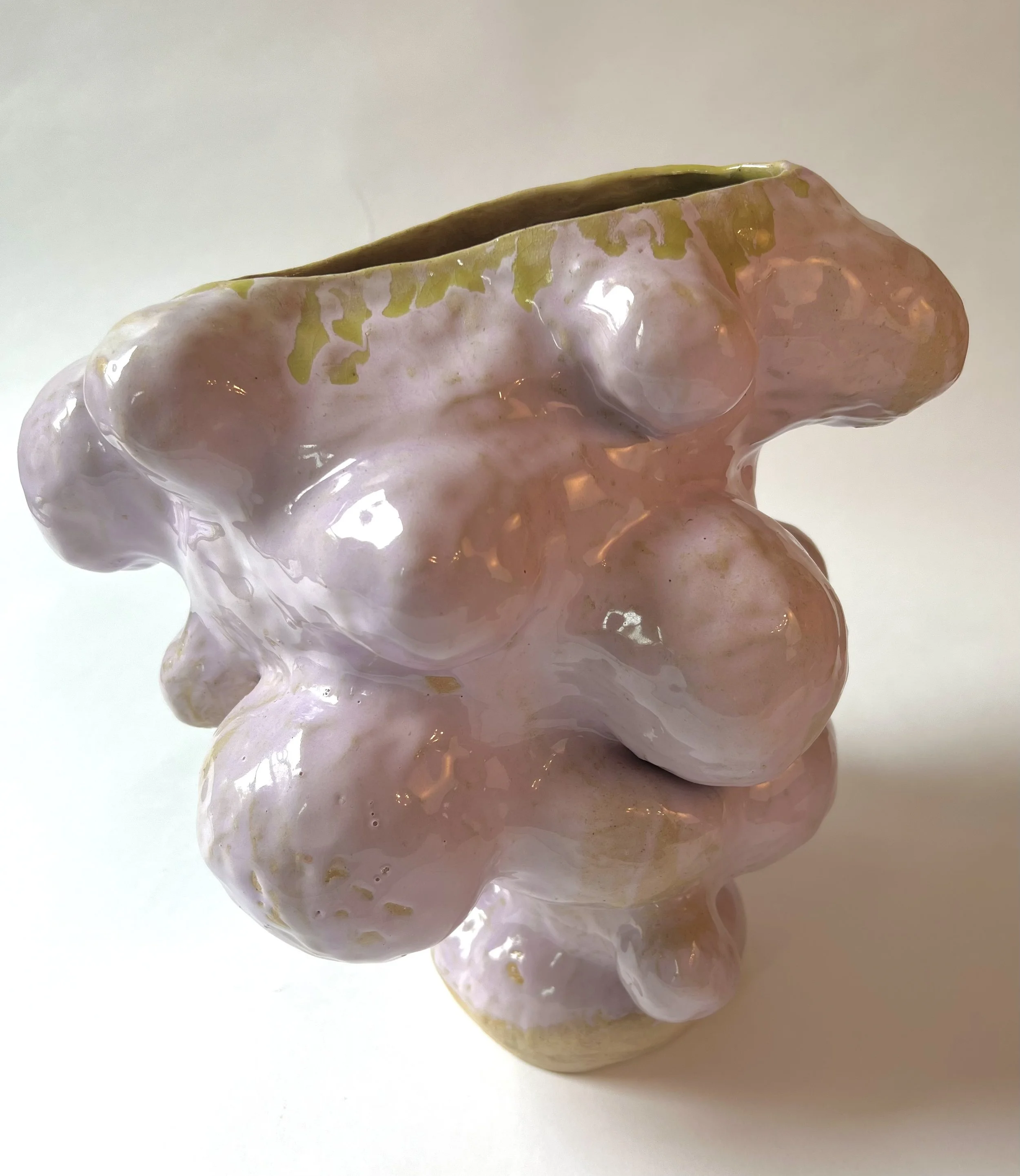 Close-up photo of a glossy pink and beige abstract sculpture with a greenish top, set against a plain white background.