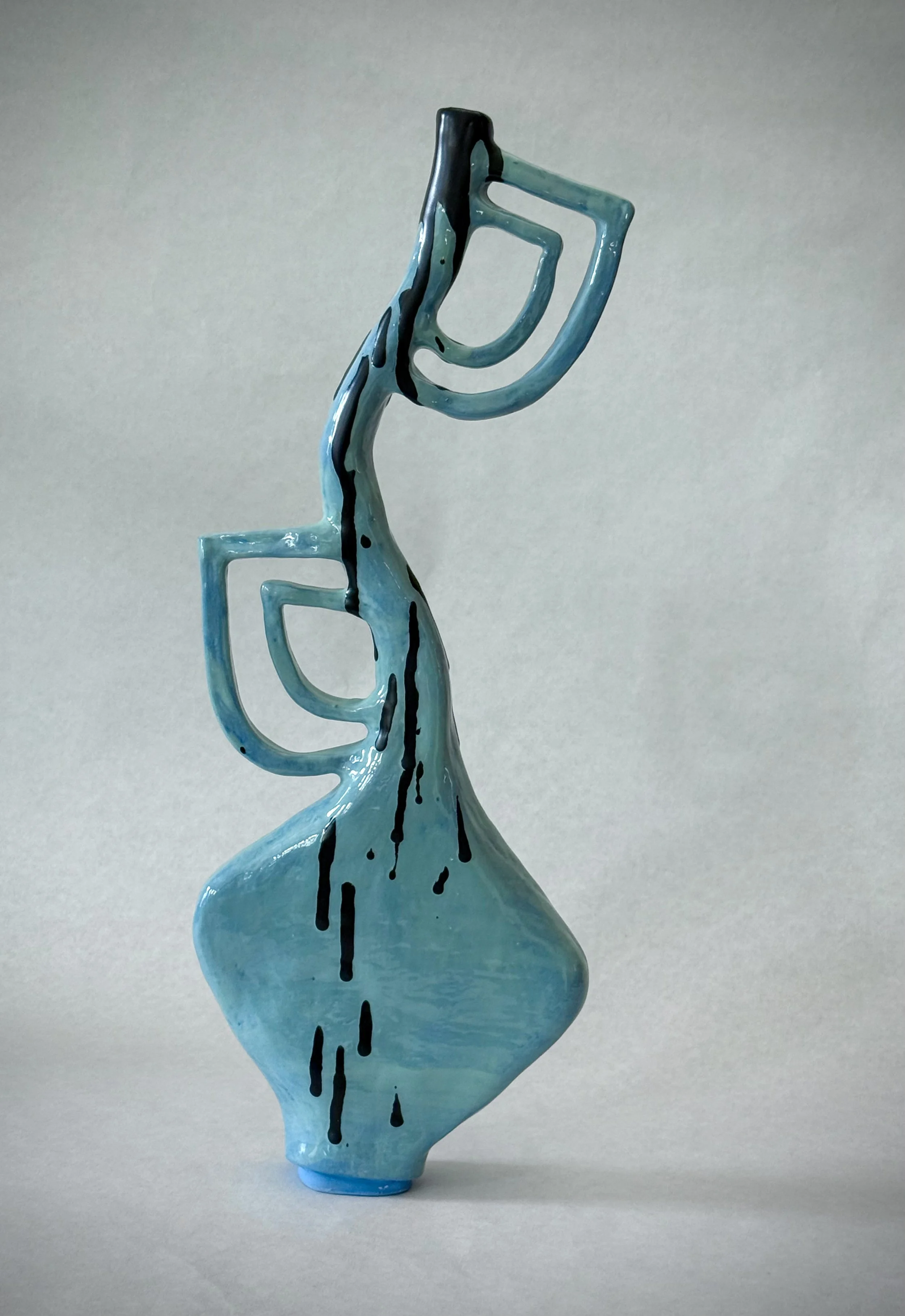 Blue ceramic vase with an abstract, modern design featuring curves and black streaks, standing on a light-colored surface against a neutral background.