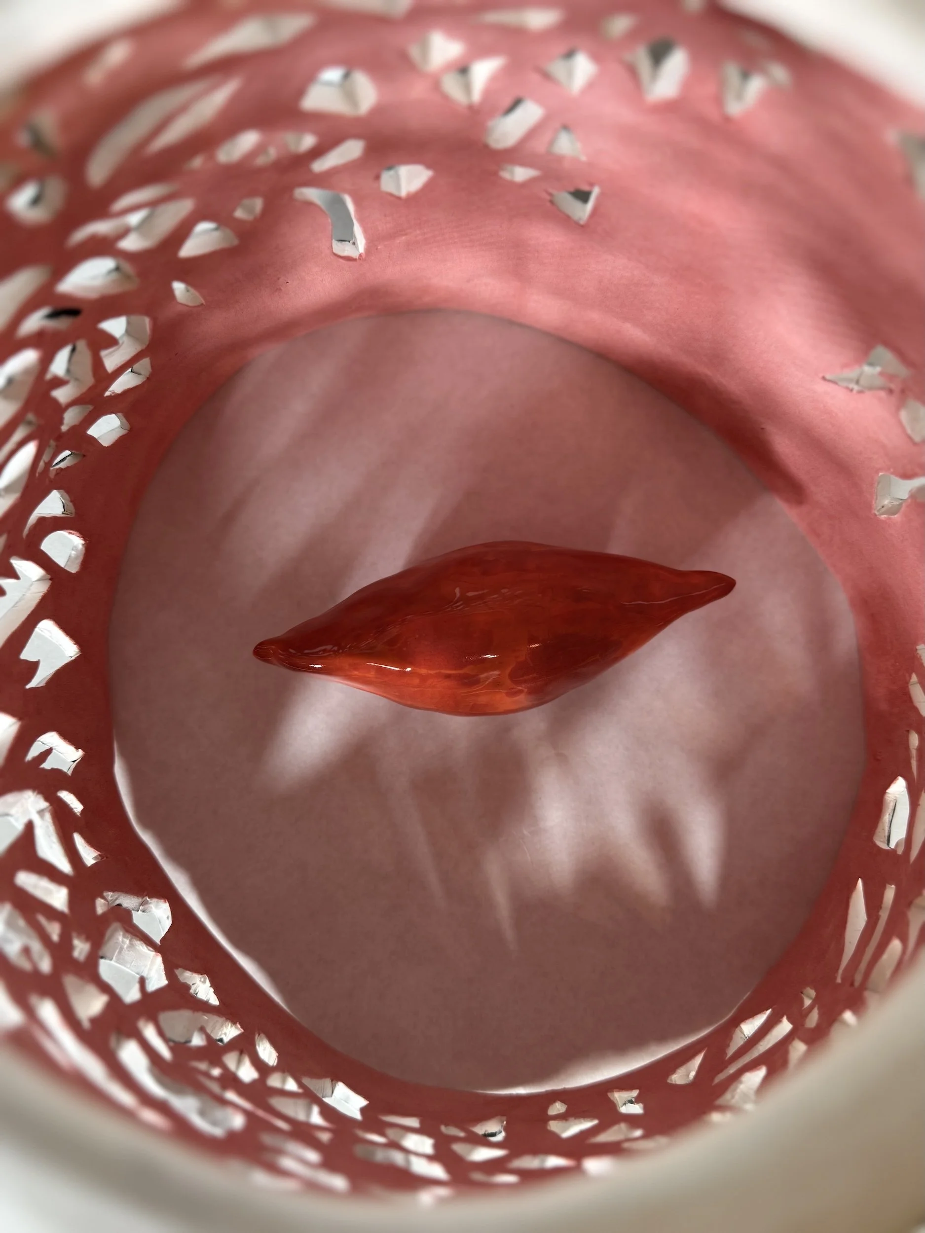 Purple and white plastic basket with holes, containing a red chili pepper and some green vegetables.